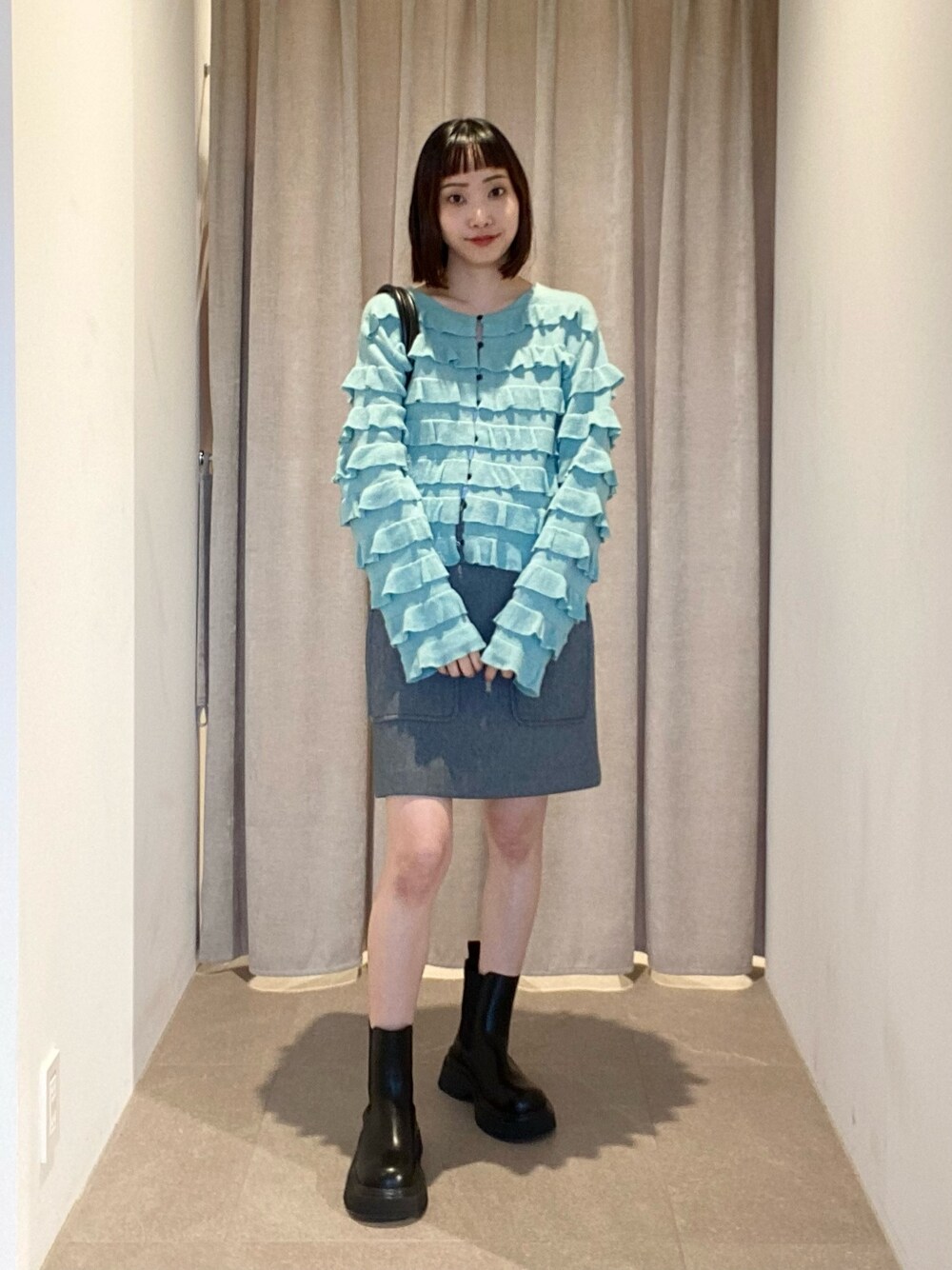 グリーン系のカーディガン/ボレロ、グレー系のスカート、ブラック系のショルダーバッグを着用したレディースの夏コーディネートの1枚目の写真