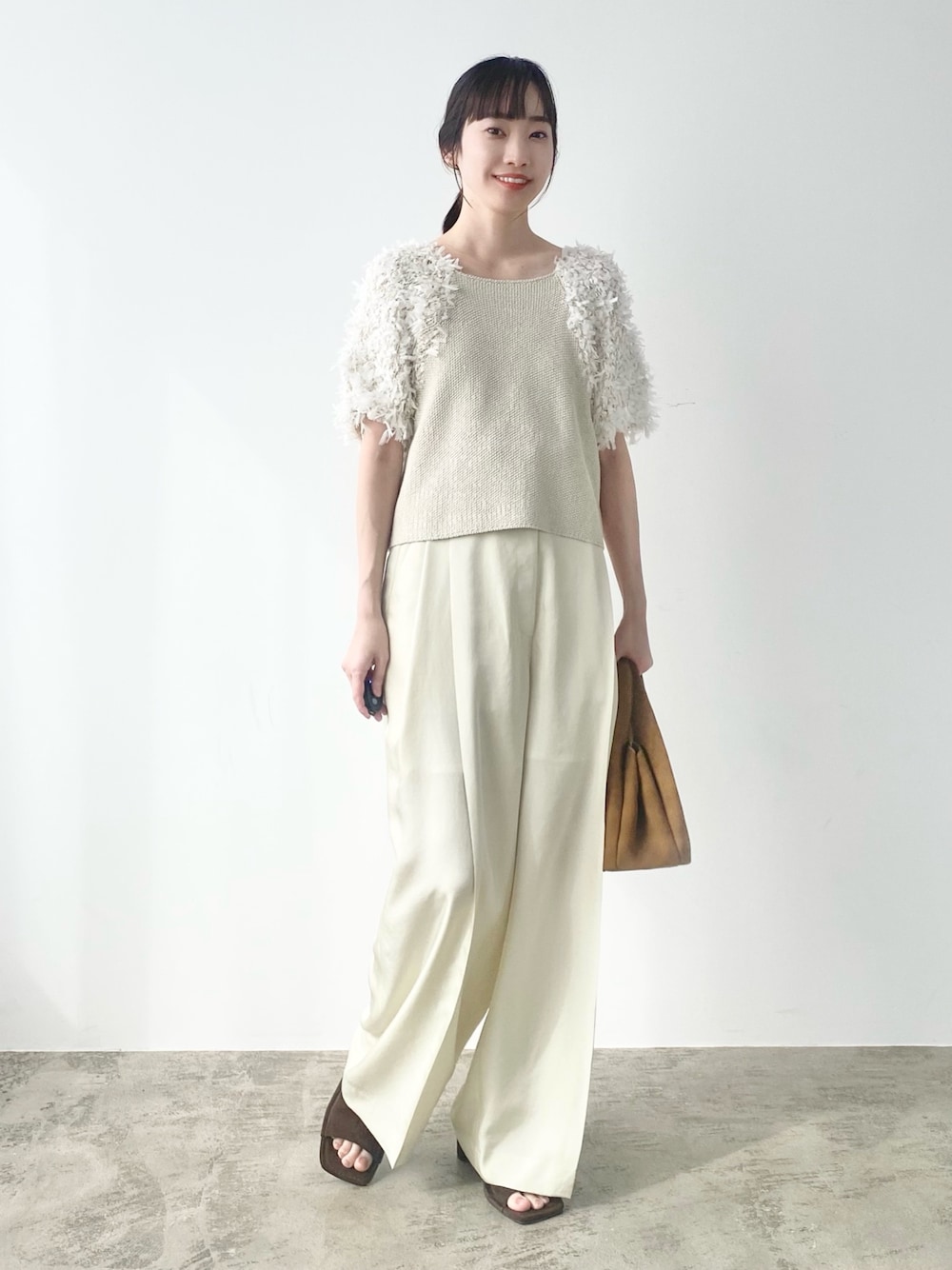 ベージュ系のニット/セーター、グリーン系のスラックス、ブラウン系のトートバッグを着用したレディースの春コーディネートの1枚目の写真