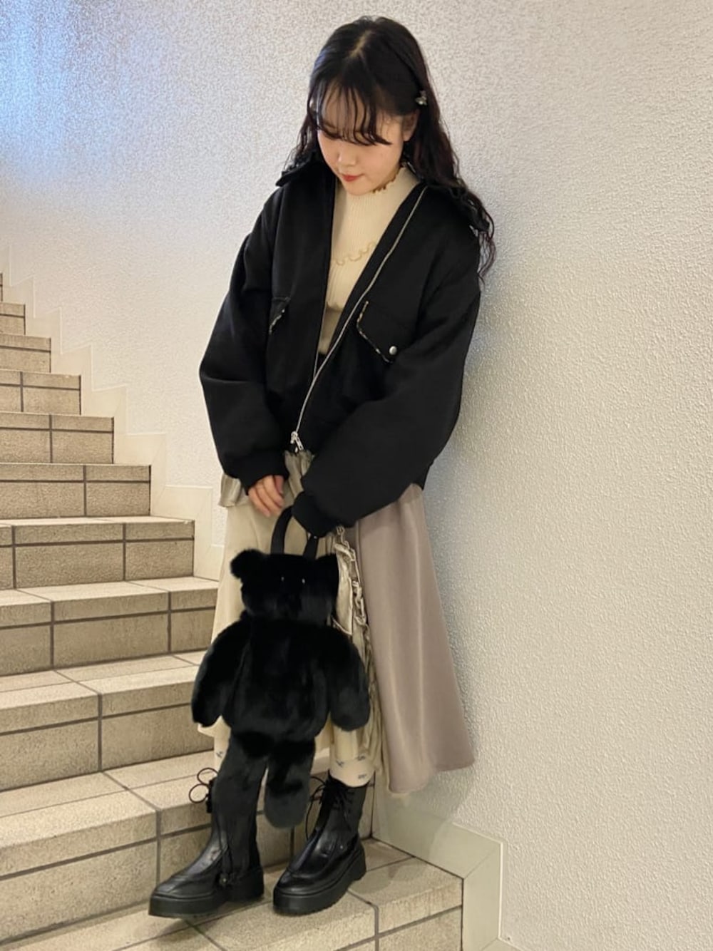 ブラック系のハンドバッグ、ブラック系のブーツ、ベージュ系のスカートを着用したレディースの冬コーディネートの1枚目の写真