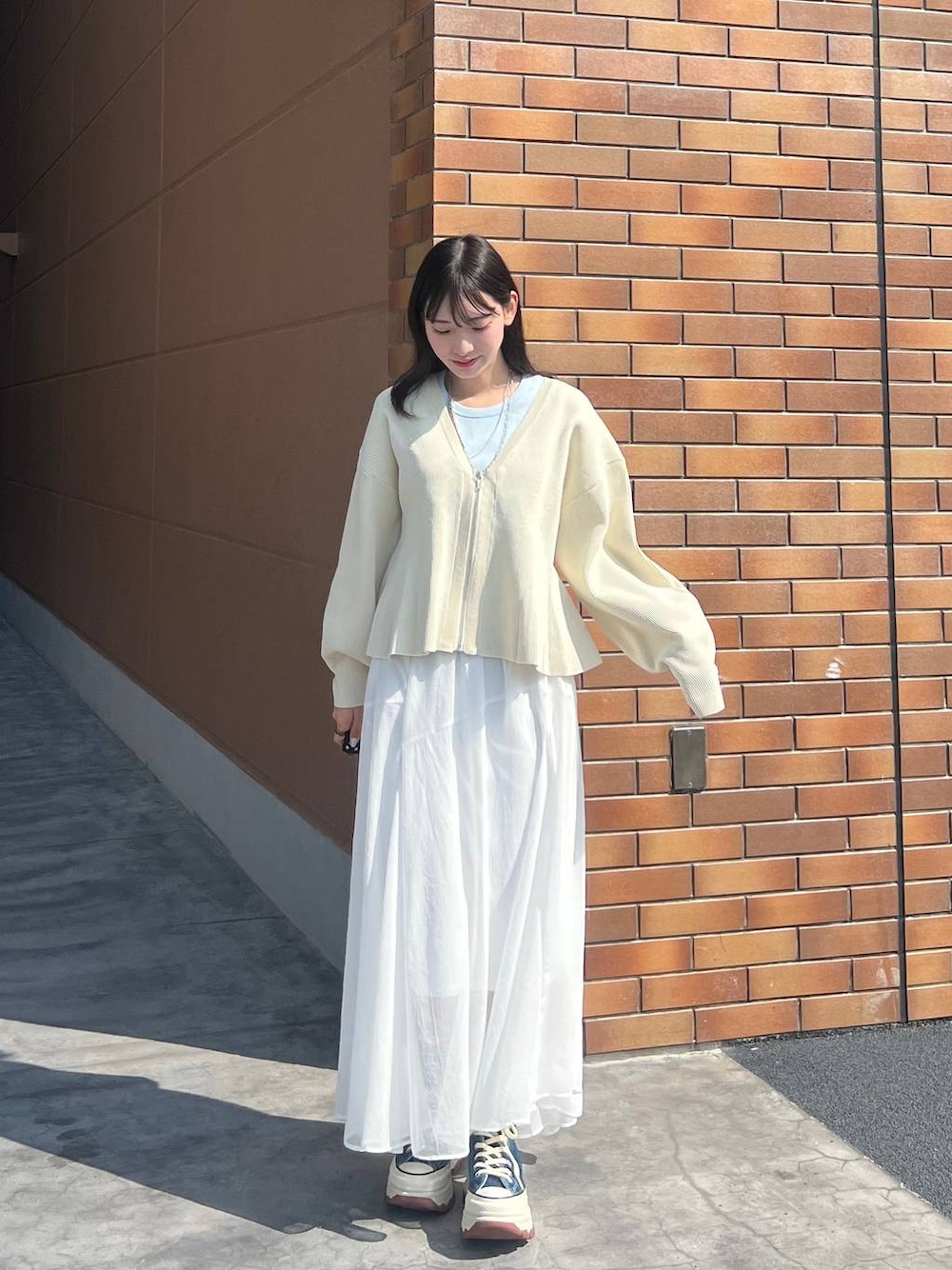 ブルー系のスニーカー、ホワイト系のカーディガン/ボレロ、ホワイト系のスカートを着用したレディースの春コーディネートの1枚目の写真