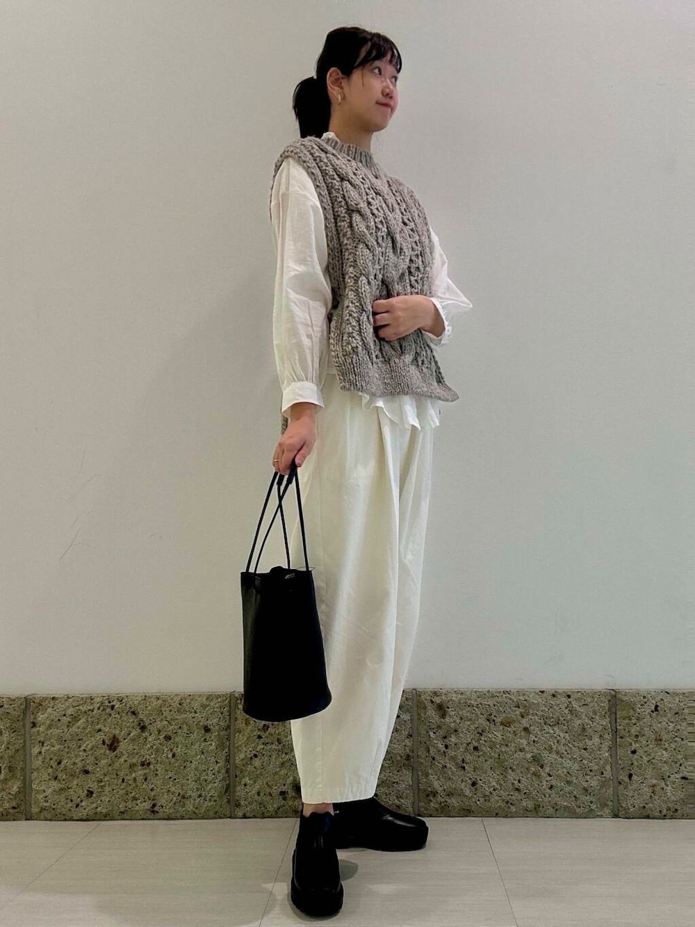 グレー系のニット/セーター、ブラック系のショルダーバッグ、ブラック系のブーツを着用したレディースの秋コーディネートの1枚目の写真