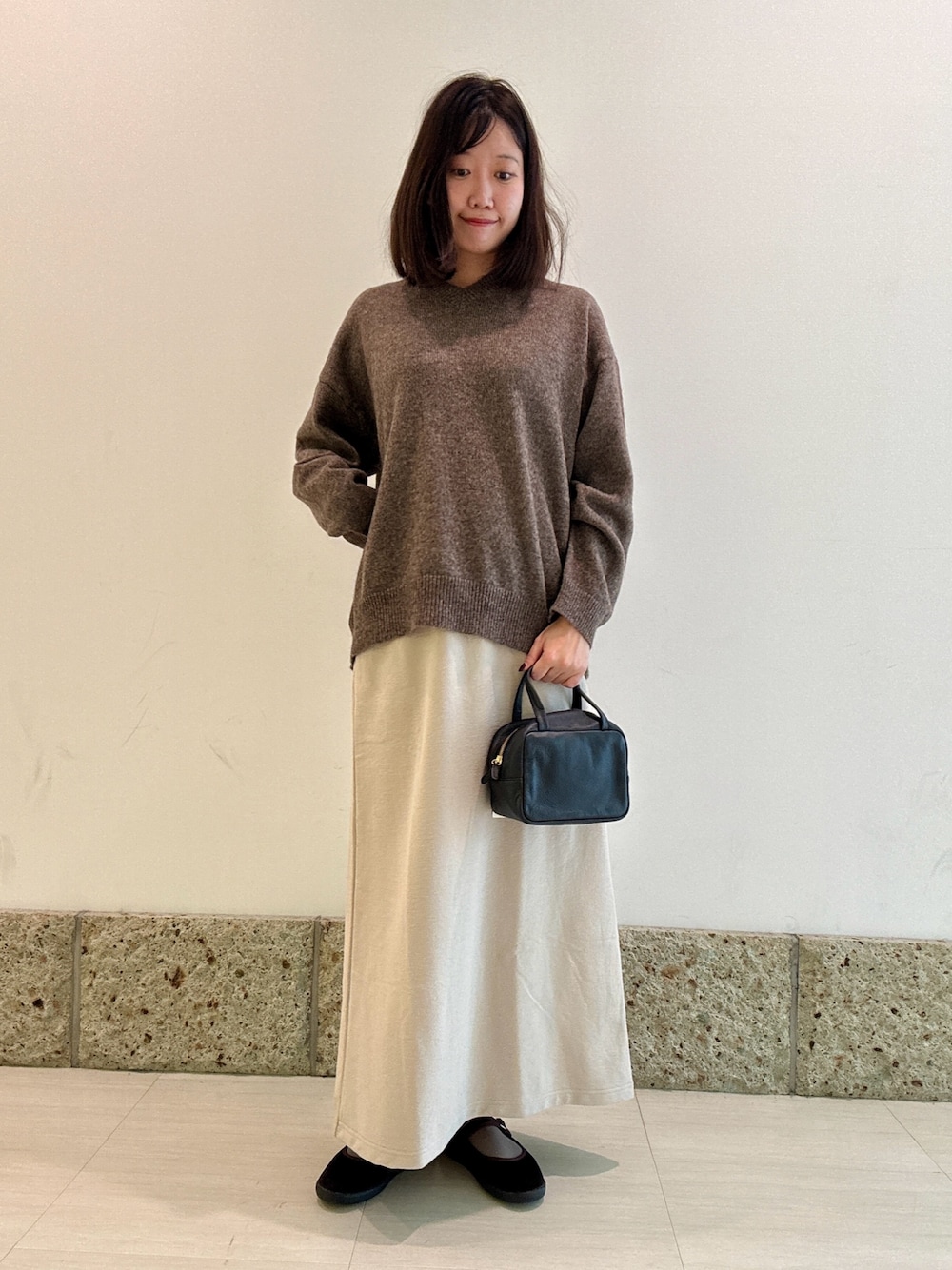 ブラック系のボストンバッグ、ブラウン系のニット/セーター、ベージュ系のスカートを着用したレディースの秋コーディネートの1枚目の写真
