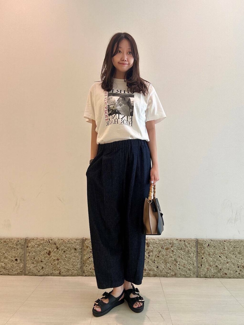 ブラック系のショルダーバッグ、ブラック系のサンダル、ホワイト系のTシャツ/カットソーを着用したレディースの夏コーディネートの1枚目の写真