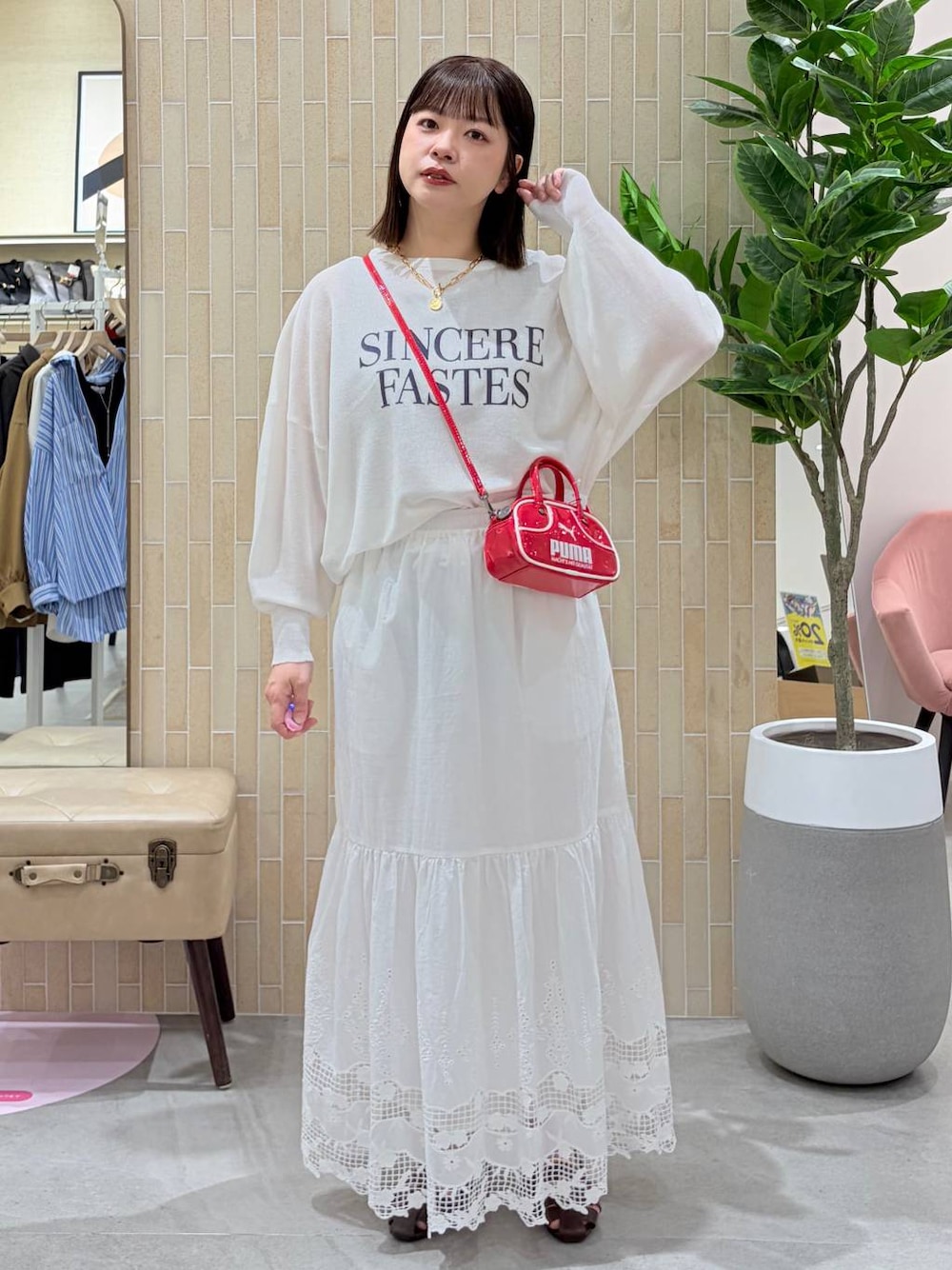 レッド系のハンドバッグ、ブラウン系のパンプス、ホワイト系のスカートを着用したレディースの春コーディネートの1枚目の写真