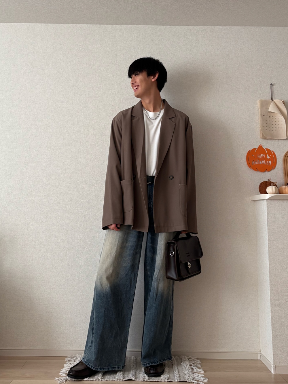 ブラウン系のショルダーバッグ、ベージュ系のその他アウター、ブルー系のデニムパンツを着用したメンズの秋コーディネートの1枚目の写真