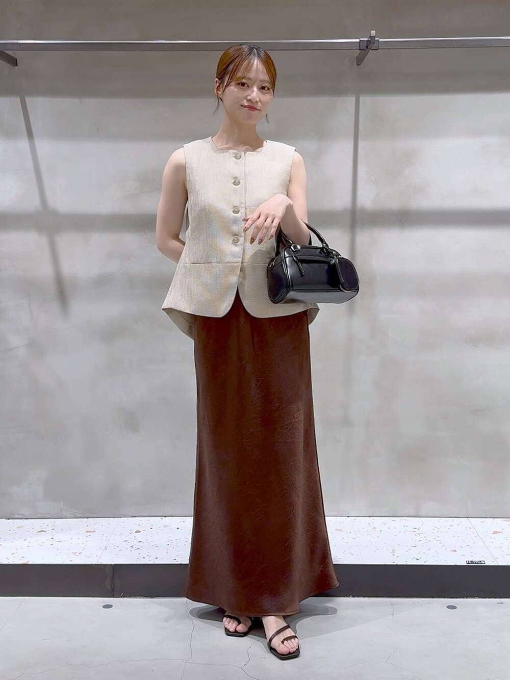 ブラウン系のスカート、ベージュ系のブルゾン、ブラック系のサンダルを着用したレディースの夏コーディネートの1枚目の写真