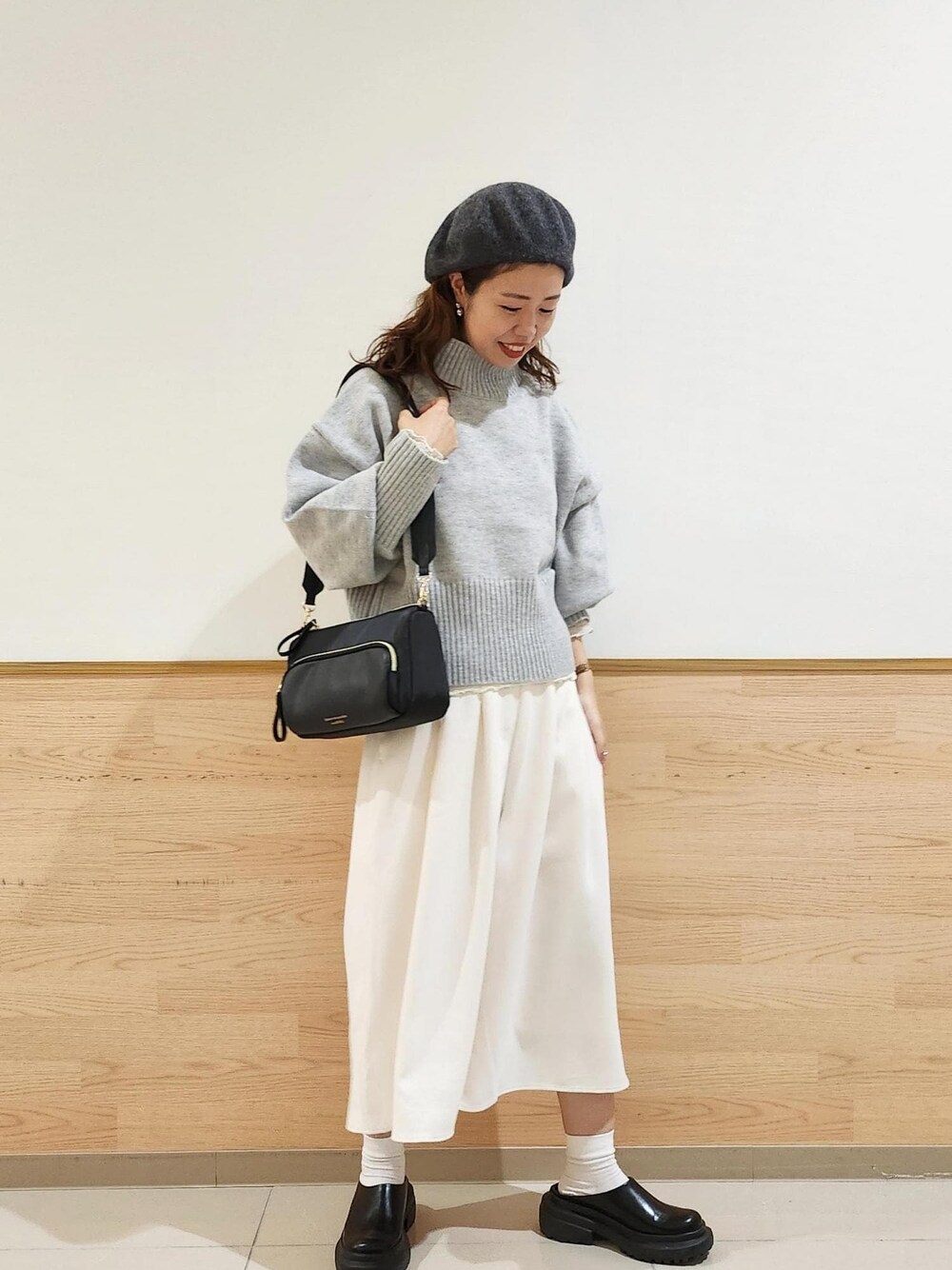 グレー系のニット/セーター、ブラック系のショルダーバッグ、ホワイト系のTシャツ/カットソーを着用したレディースの秋コーディネートの1枚目の写真