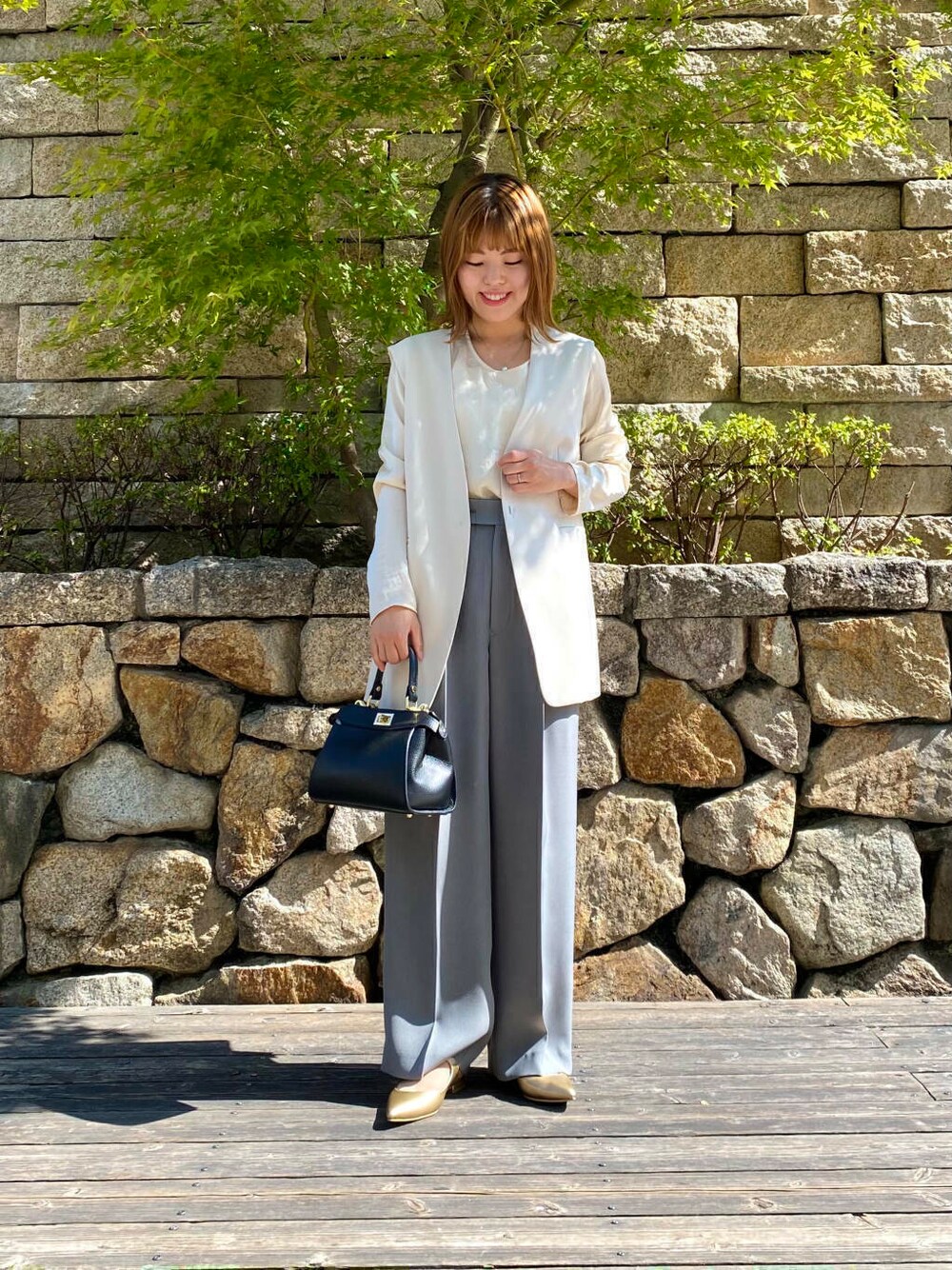 ブラック系のハンドバッグ、ゴールド系のパンプス、グレー系のその他パンツを着用したレディースの夏コーディネートの1枚目の写真