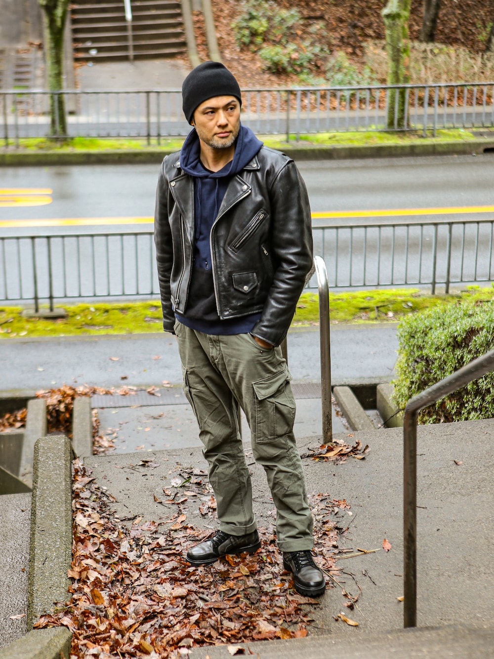 ブルー系のパーカー、ブラック系のライダースジャケット、グリーン系のカーゴパンツを着用したメンズの冬コーディネートの1枚目の写真