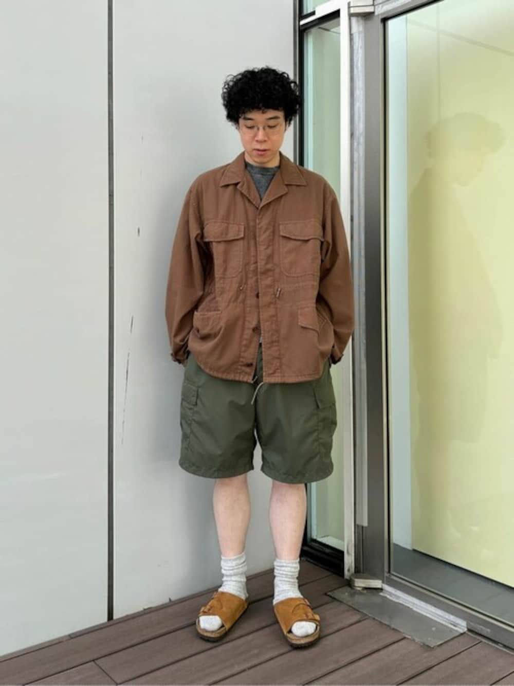 ブラウン系のサンダル、ブラウン系のダウンジャケット/コート、グリーン系のカーゴパンツを着用したメンズの夏コーディネートの1枚目の写真