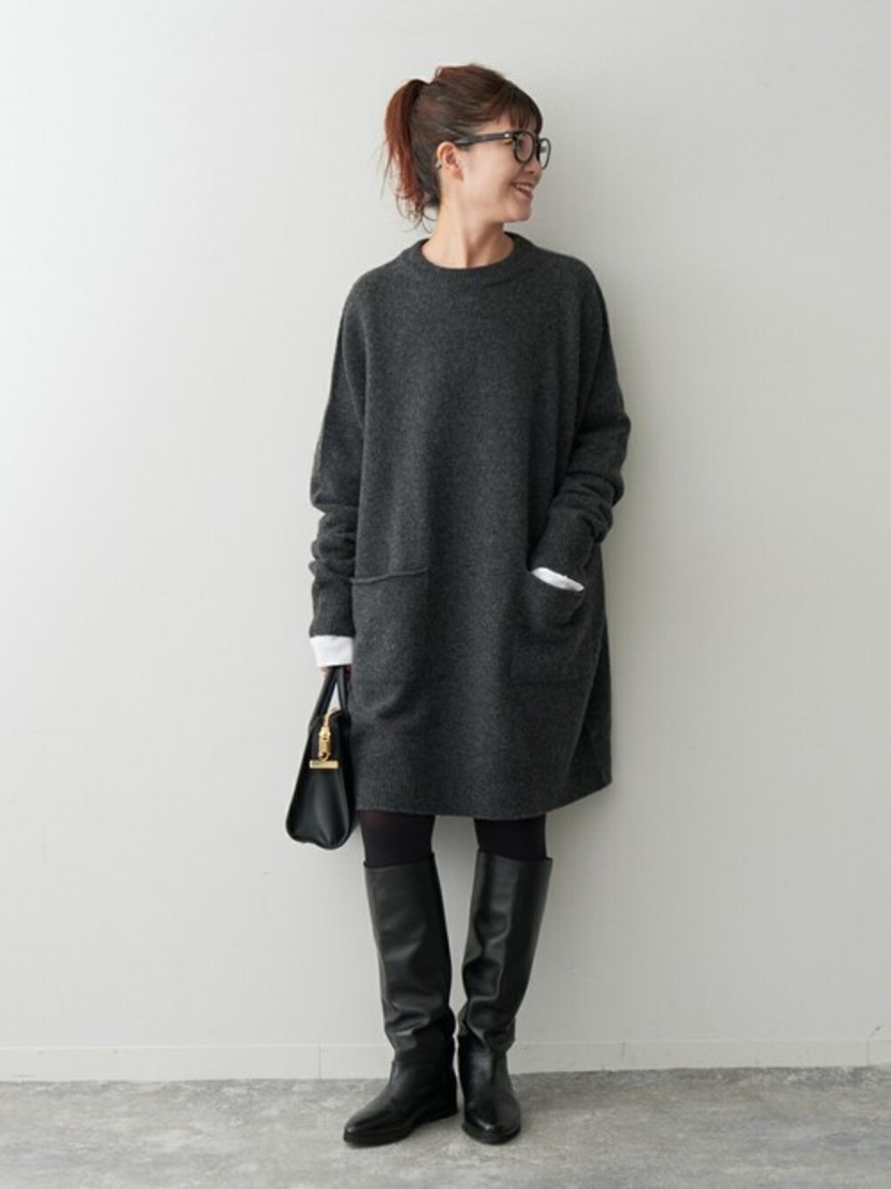 グレー系のニット/セーター、ブラック系のボストンバッグ、ブラック系のブーツを着用したレディースの秋コーディネートの1枚目の写真