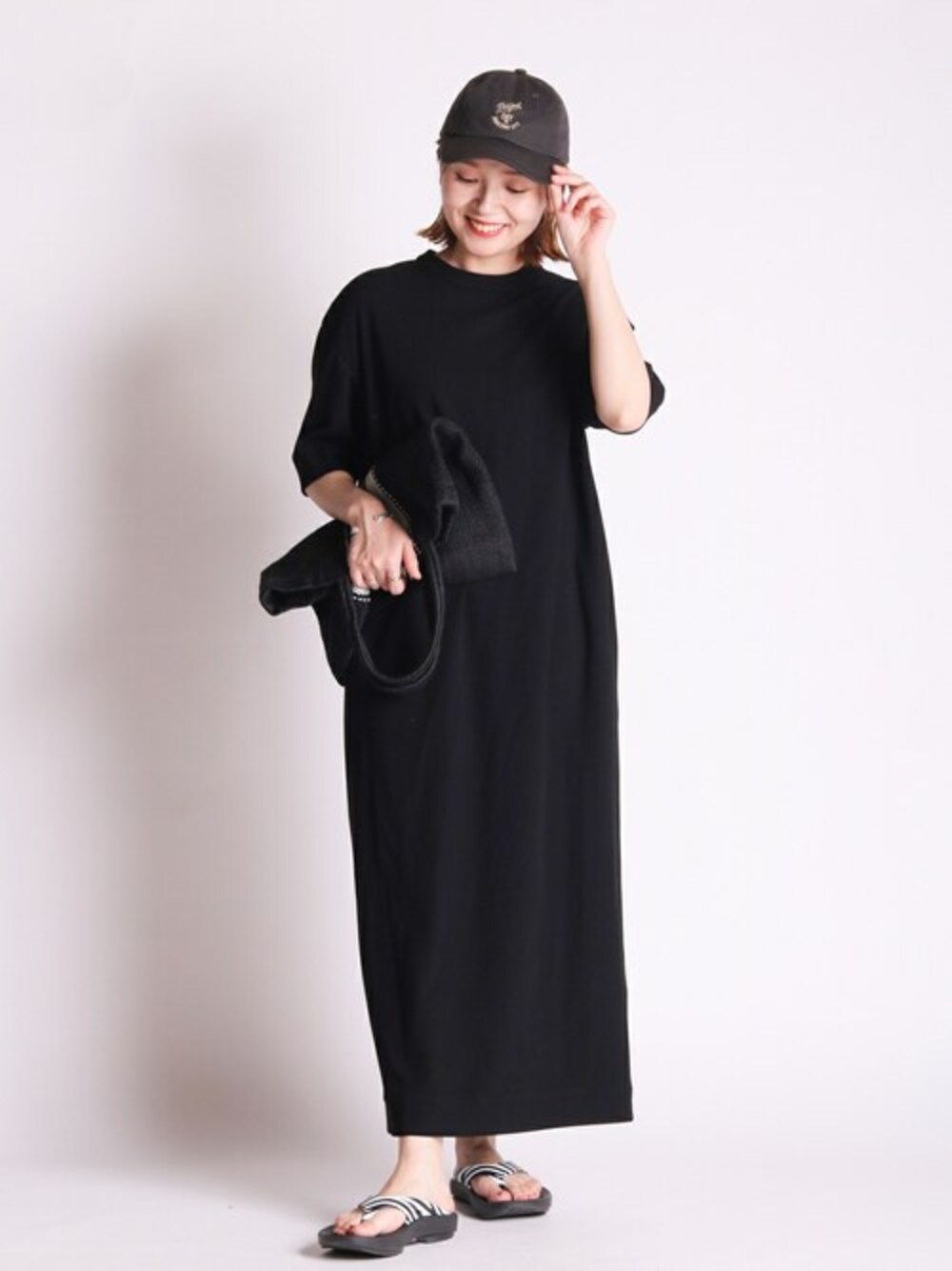 ブラック系のワンピース、ホワイト系のトートバッグ、ホワイト系のサンダルを着用したレディースの夏コーディネートの1枚目の写真