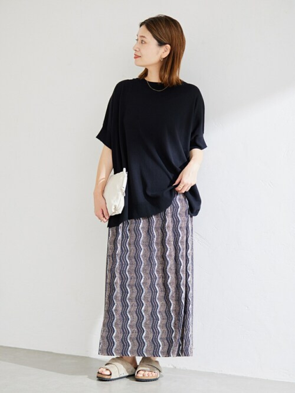 ブラウン系のスカート、ホワイト系のショルダーバッグ、ベージュ系のサンダルを着用したレディースの夏コーディネートの1枚目の写真