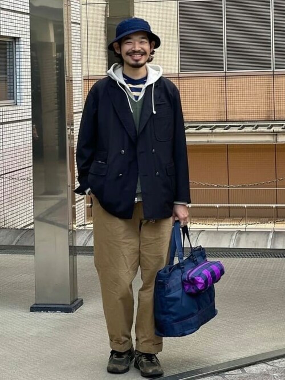 ベージュ系のスウェット、ブラウン系のチノパンツ、ブルー系のトートバッグを着用したメンズの春コーディネートの1枚目の写真