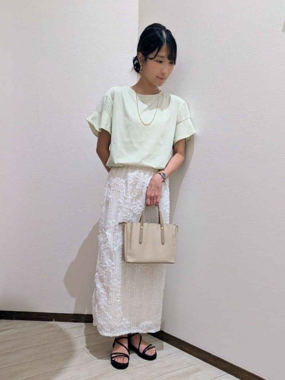 グリーン系のTシャツ/カットソー、ホワイト系のスカート、ブラック系のサンダルを着用したレディースの夏コーディネートの1枚目の写真