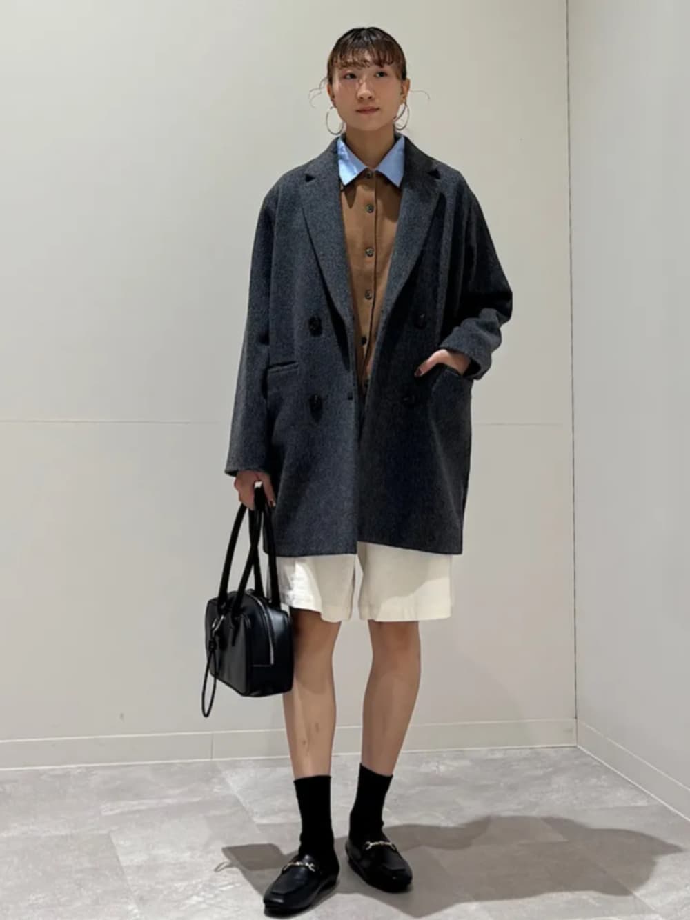 グレー系のチェスターコート、イエロー系のカーディガン/ボレロ、ブラック系のショルダーバッグを着用したレディースの秋コーディネートの1枚目の写真