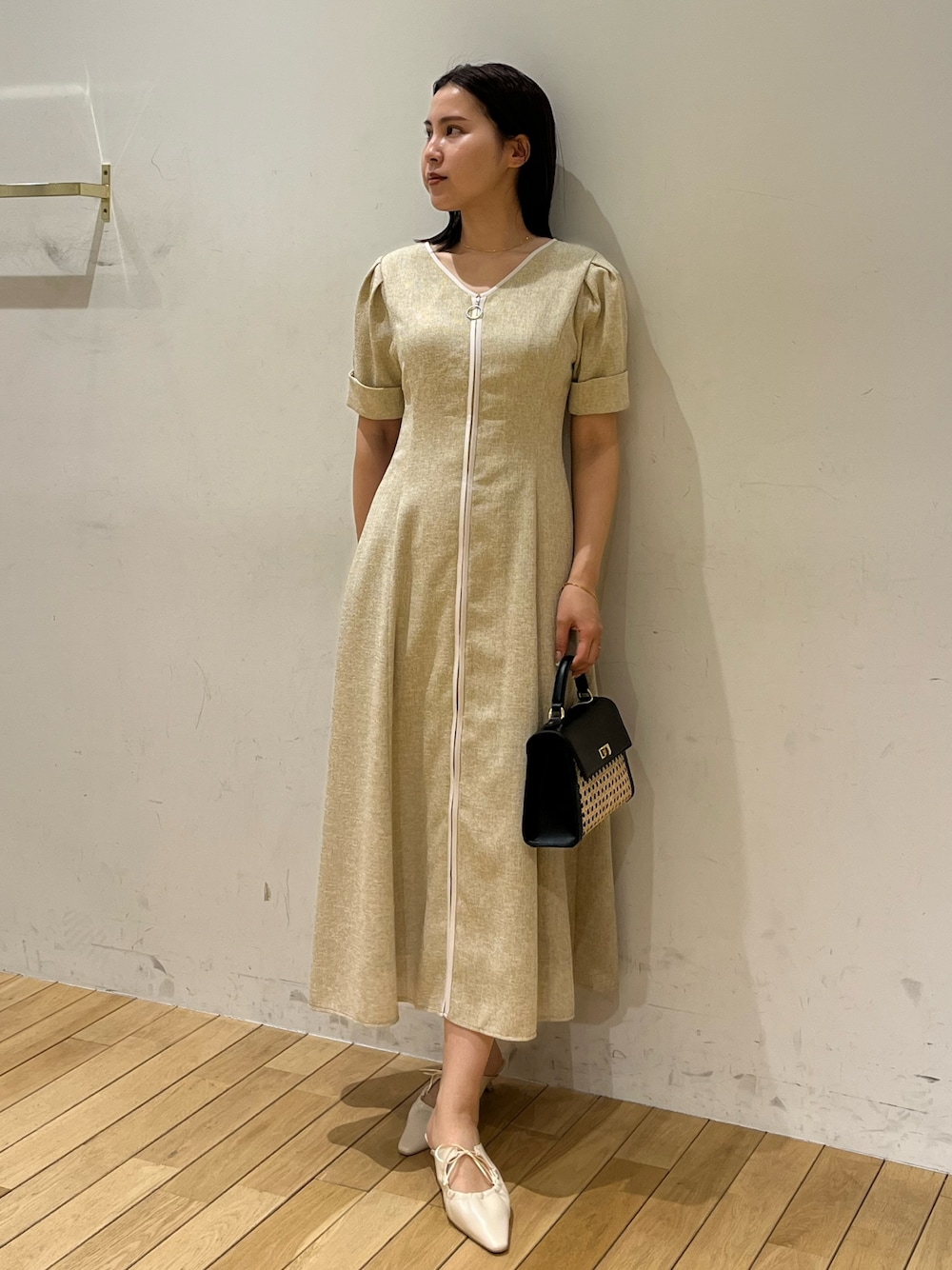 ベージュ系のワンピース、ホワイト系のサンダル、ブラック系のハンドバッグを着用したレディースの春コーディネートの1枚目の写真