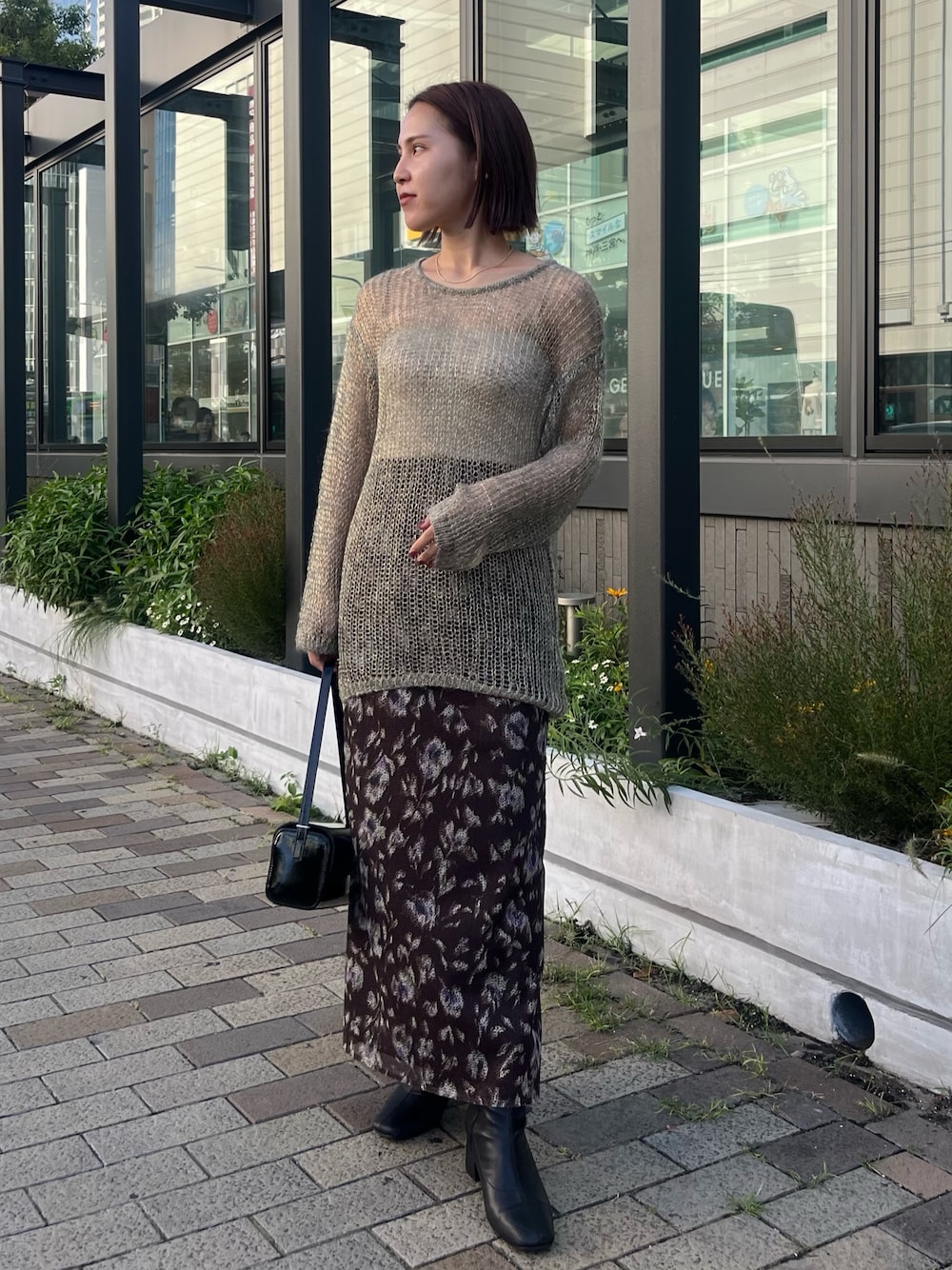 ブラック系のショルダーバッグ、グレー系のニット/セーター、ブラウン系のスカートを着用したレディースの秋コーディネートの1枚目の写真