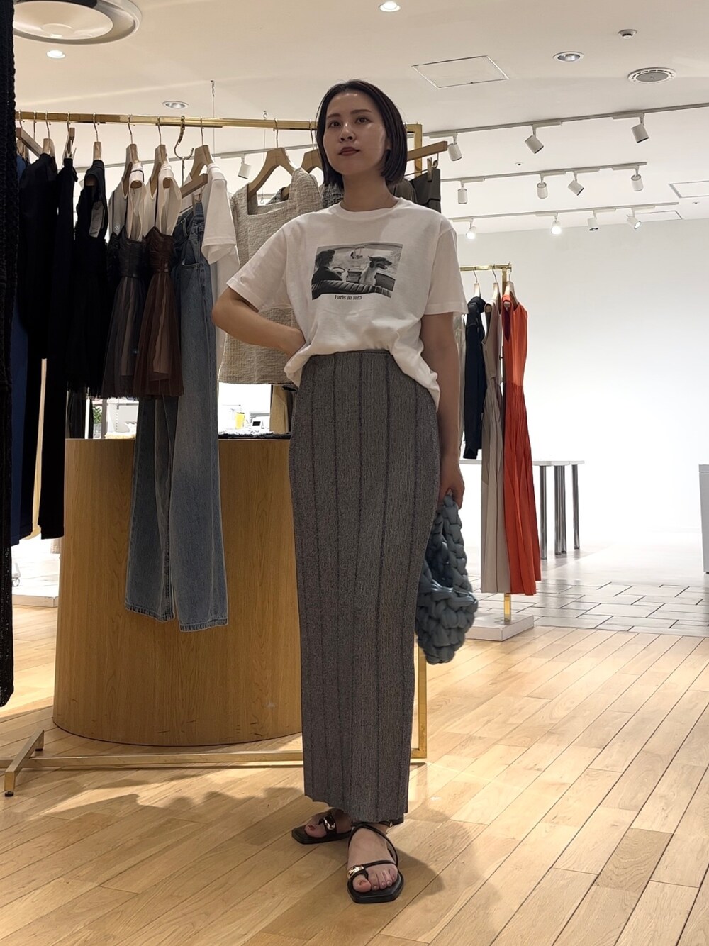 グレー系のスカート、ブラック系のサンダル、ブルー系のハンドバッグを着用したレディースの夏コーディネートの1枚目の写真