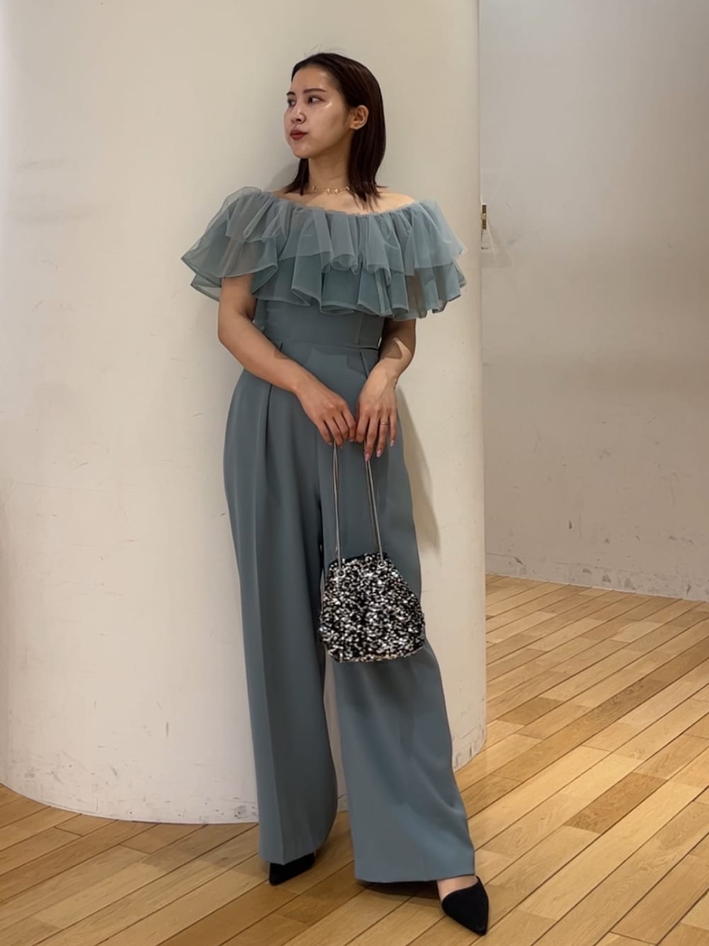 シルバー系のショルダーバッグ、ブラック系のパンプス、ブルー系のパンツドレスを着用したレディースの春コーディネートの1枚目の写真