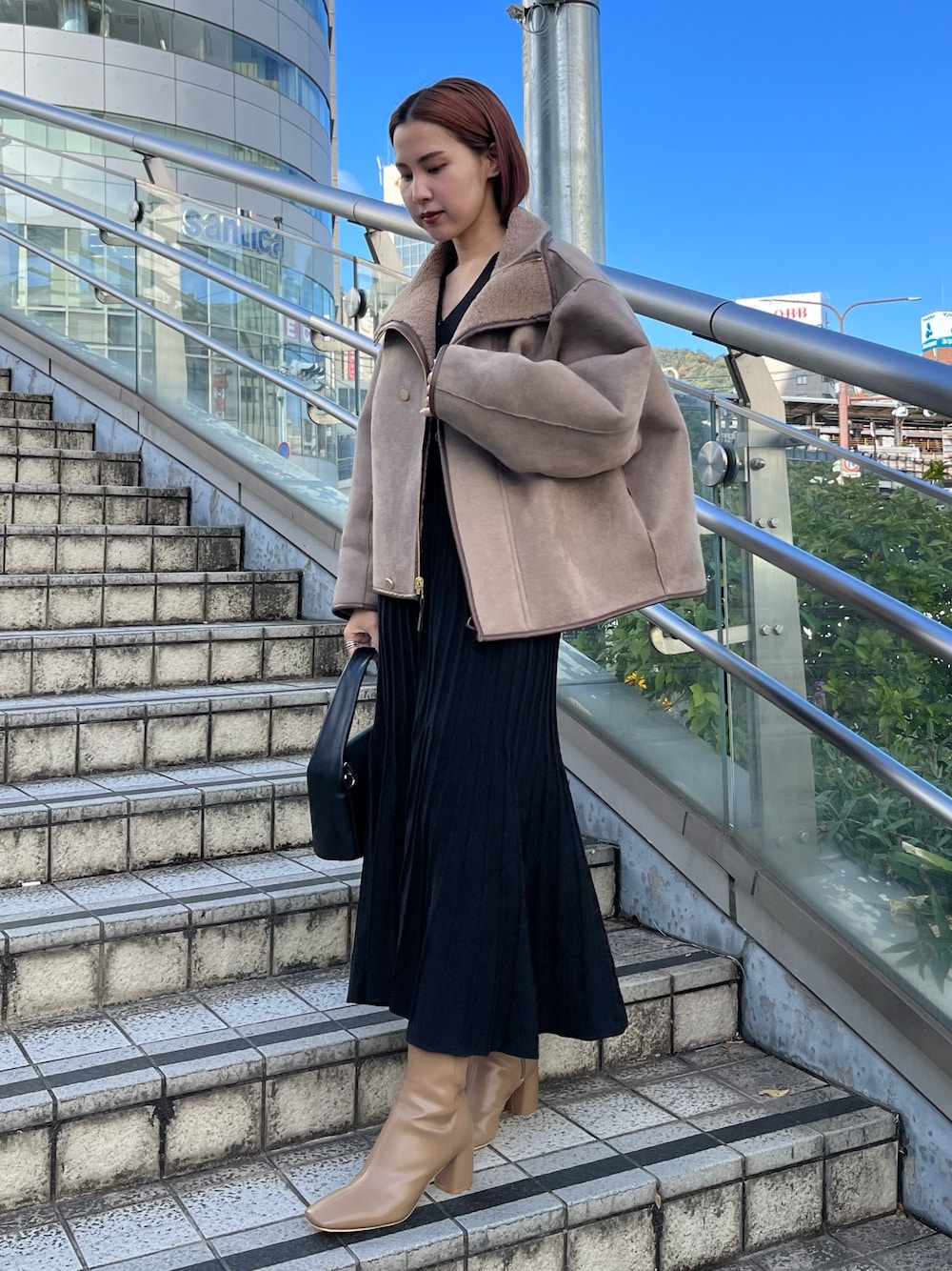 ブラック系のワンピース、ベージュ系のブーツ、ブラック系のハンドバッグを着用したレディースの秋コーディネートの1枚目の写真