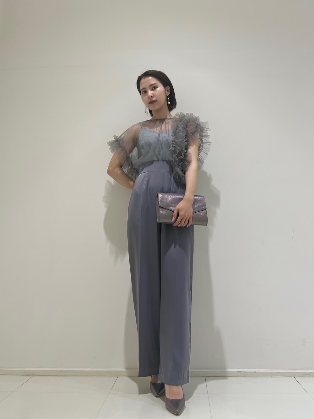 シルバー系のハンドバッグ、シルバー系のパンプス、グレー系のパンツドレスを着用したレディースの春コーディネートの1枚目の写真