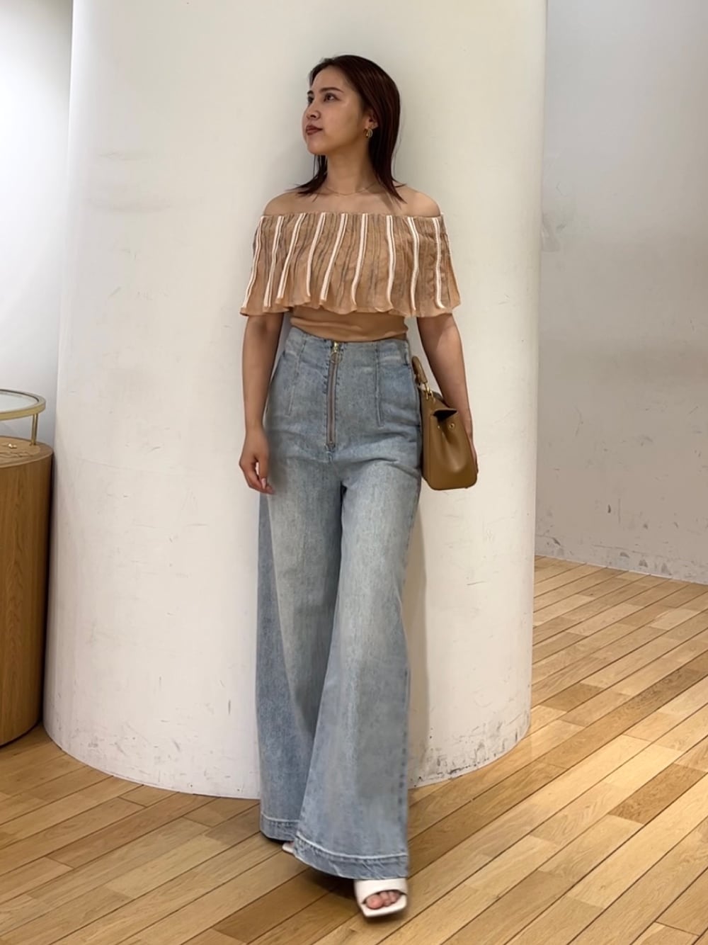 ブルー系のデニムパンツ、ホワイト系のサンダル、ブラウン系のハンドバッグを着用したレディースの春コーディネートの1枚目の写真