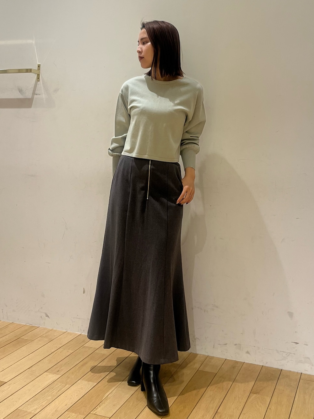 グリーン系のニット/セーター、グレー系のスカート、ブラック系のブーツを着用したレディースの冬コーディネートの1枚目の写真