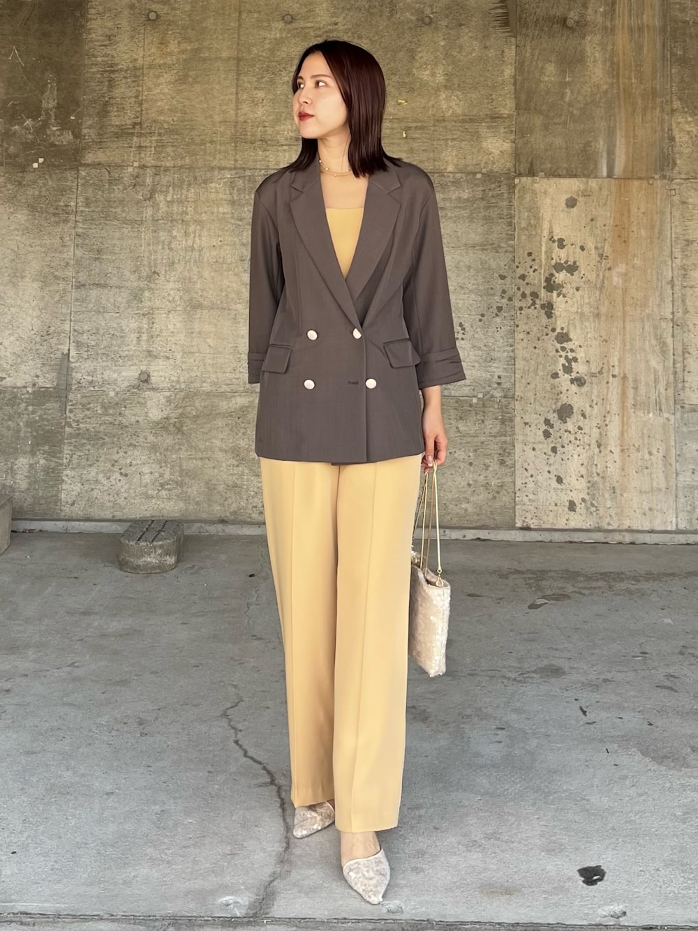 イエロー系のパンツドレス、ベージュ系のパンプス、ベージュ系のショルダーバッグを着用したレディースの春コーディネートの1枚目の写真