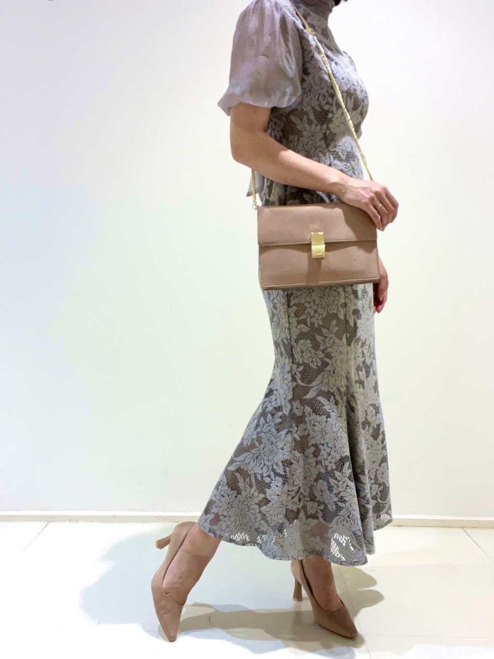 グレー系のドレス、ベージュ系のクラッチバッグ、ゴールド系のパンプスを着用したレディースの夏コーディネートの1枚目の写真