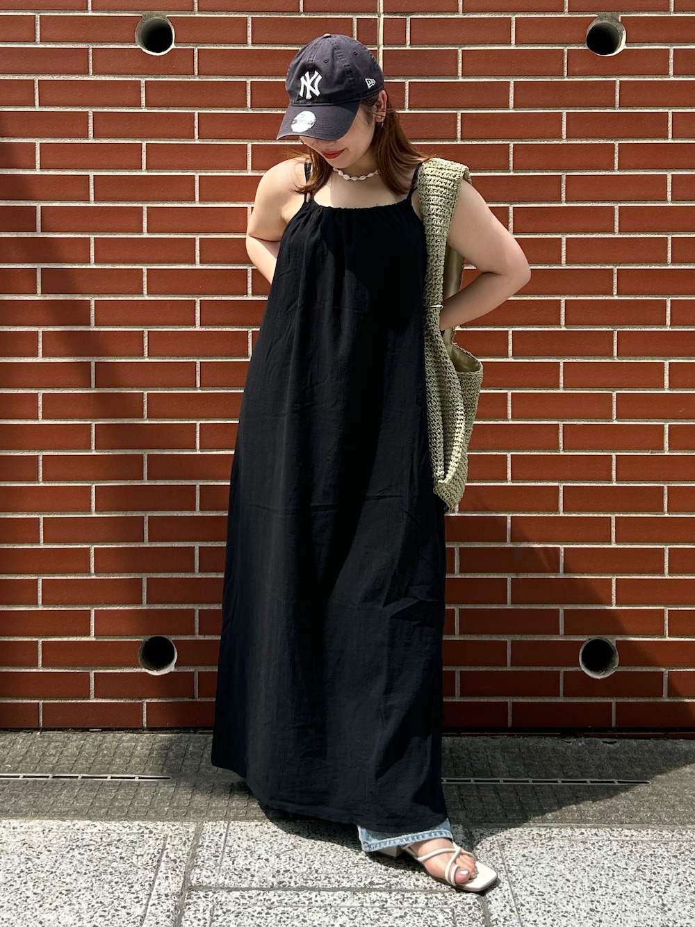 ブルー系のデニムパンツ、ブラック系のワンピース、グリーン系のショルダーバッグを着用したレディースの夏コーディネートの1枚目の写真