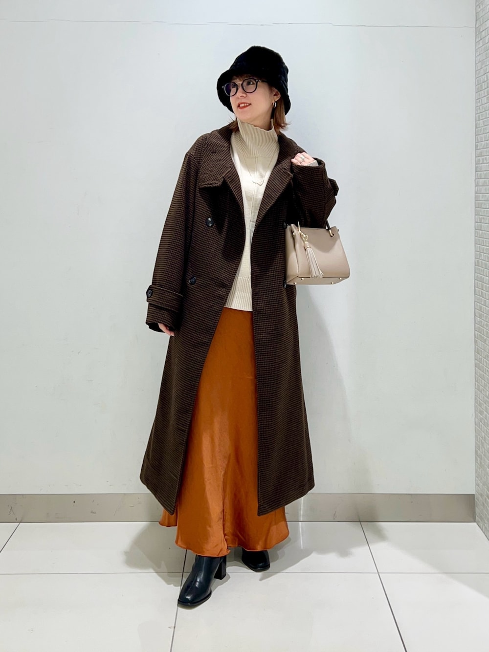ホワイト系のニット/セーター、ベージュ系のトートバッグ、ブラウン系のステンカラーコートを着用したレディースの冬コーディネートの1枚目の写真