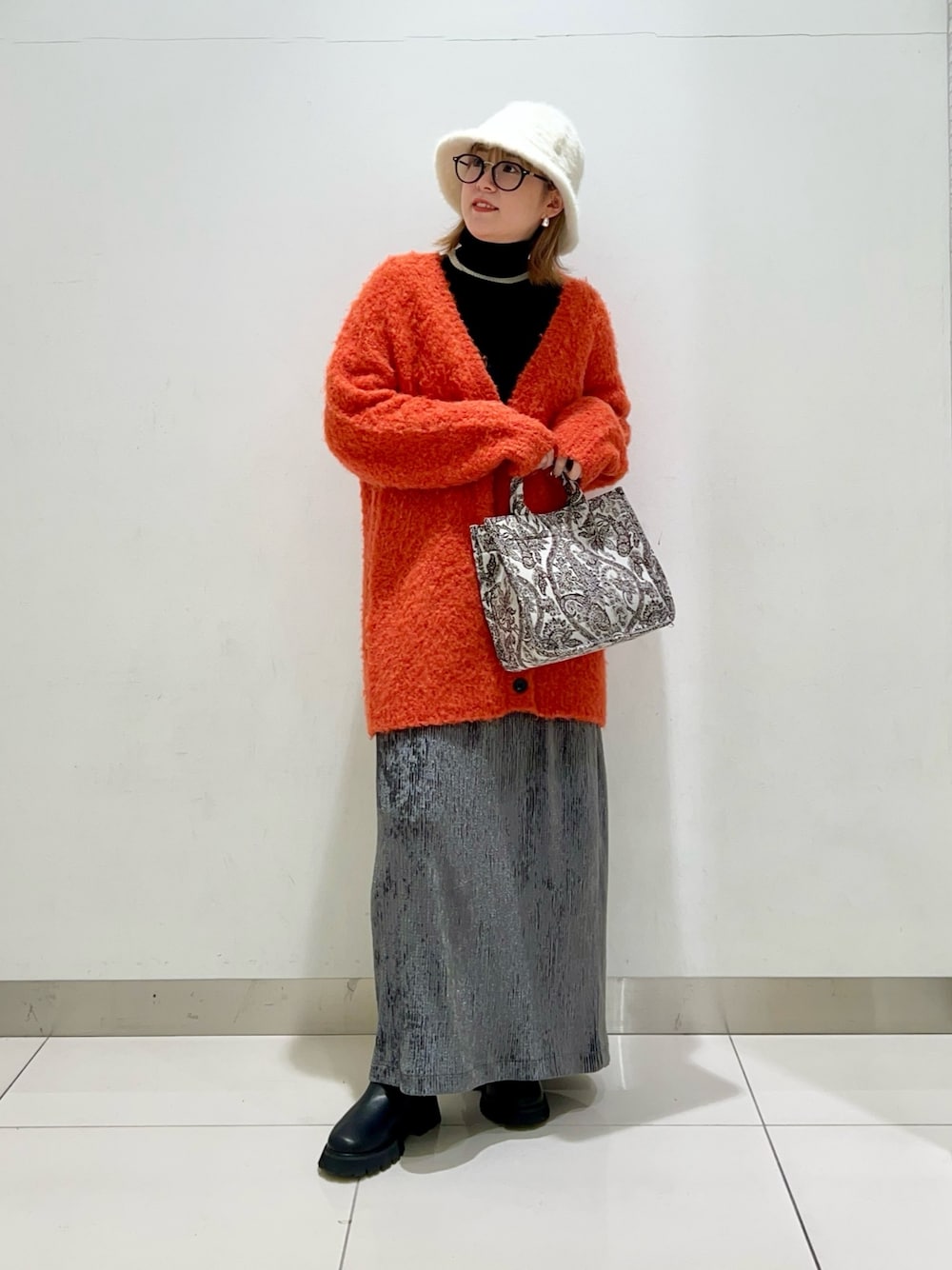 ブラック系のニット/セーター、オレンジ系のカーディガン/ボレロ、ブラウン系のトートバッグを着用したレディースの冬コーディネートの1枚目の写真