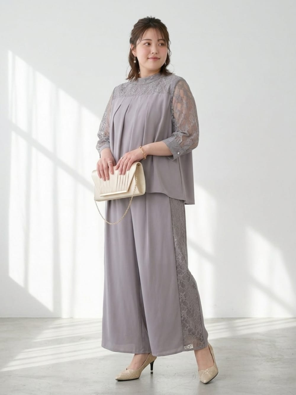 ゴールド系のバッグ、ベージュ系のパンプス、グレー系のパンツドレスを着用したレディースの秋コーディネートの1枚目の写真