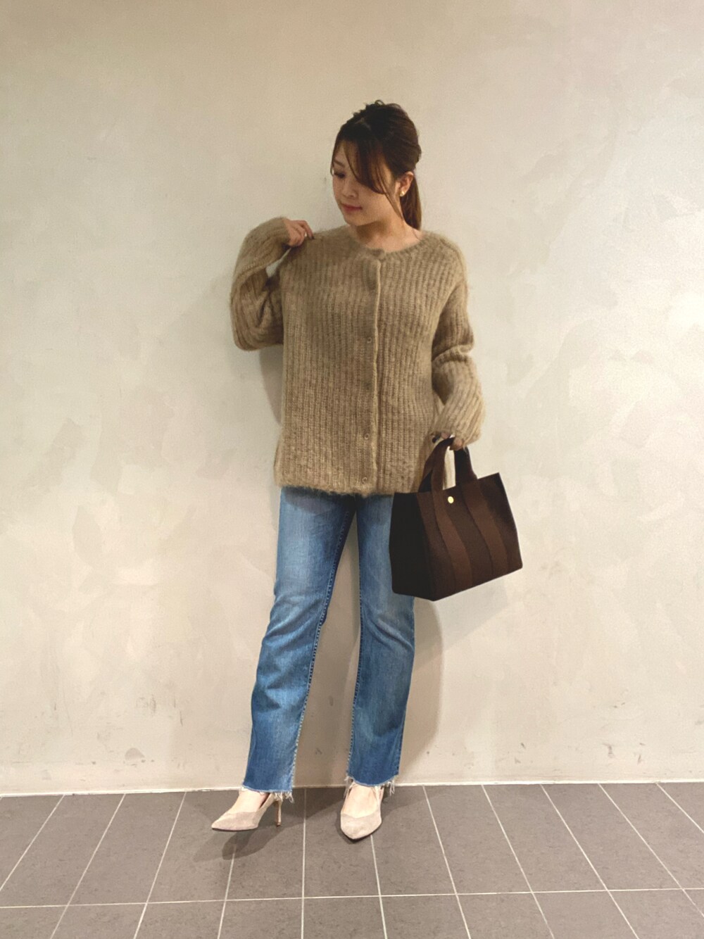 ブルー系のデニムパンツ、ブラウン系のトートバッグ、ベージュ系のニット/セーターを着用したレディースの冬コーディネートの1枚目の写真