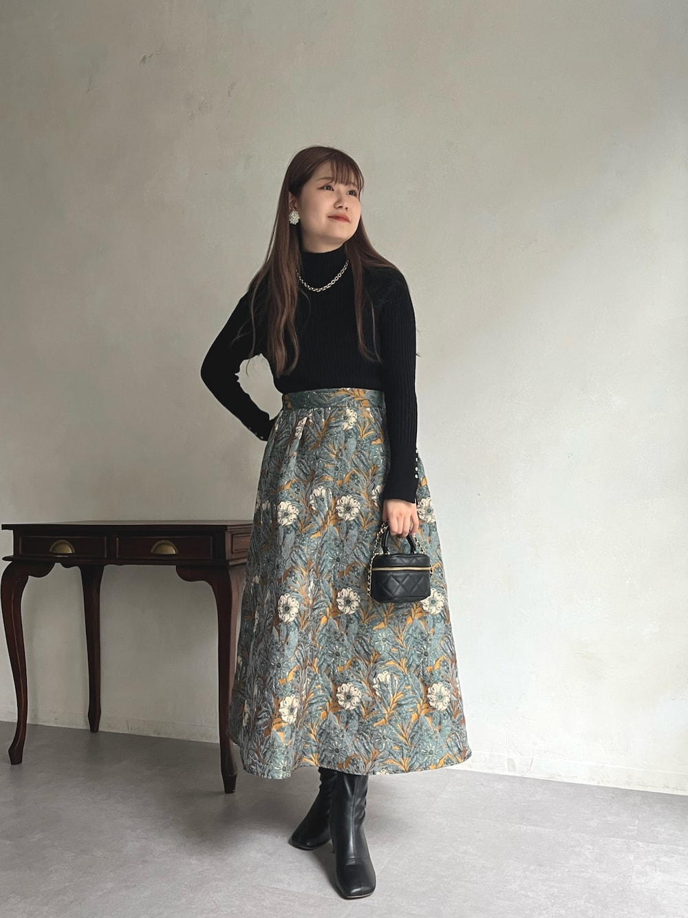 イエロー系のスカート、ブラック系のニット/セーター、ブラック系のショルダーバッグを着用したレディースの秋コーディネートの1枚目の写真