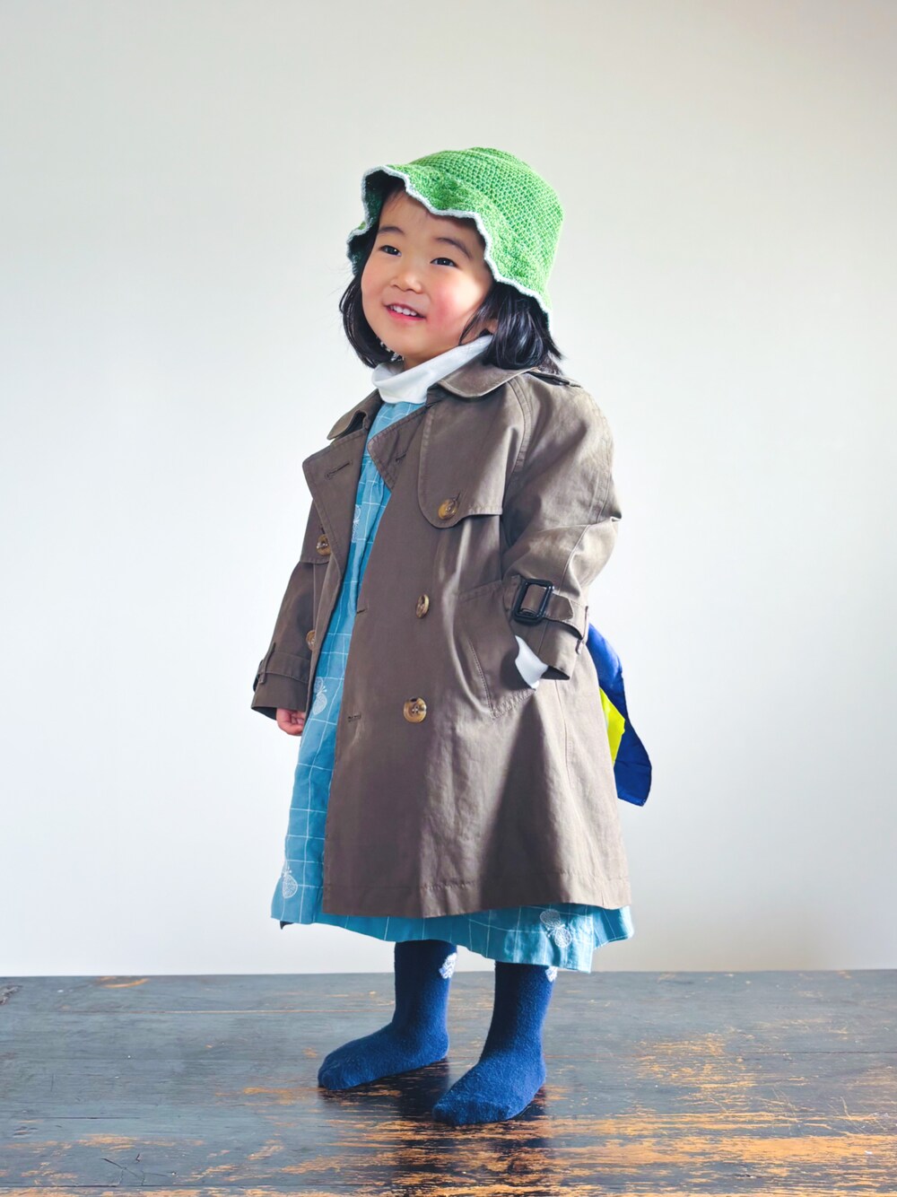 グリーン系のトレンチコート、ホワイト系のTシャツ/カットソー、ブルー系のワンピースを着用したキッズの春コーディネートの1枚目の写真