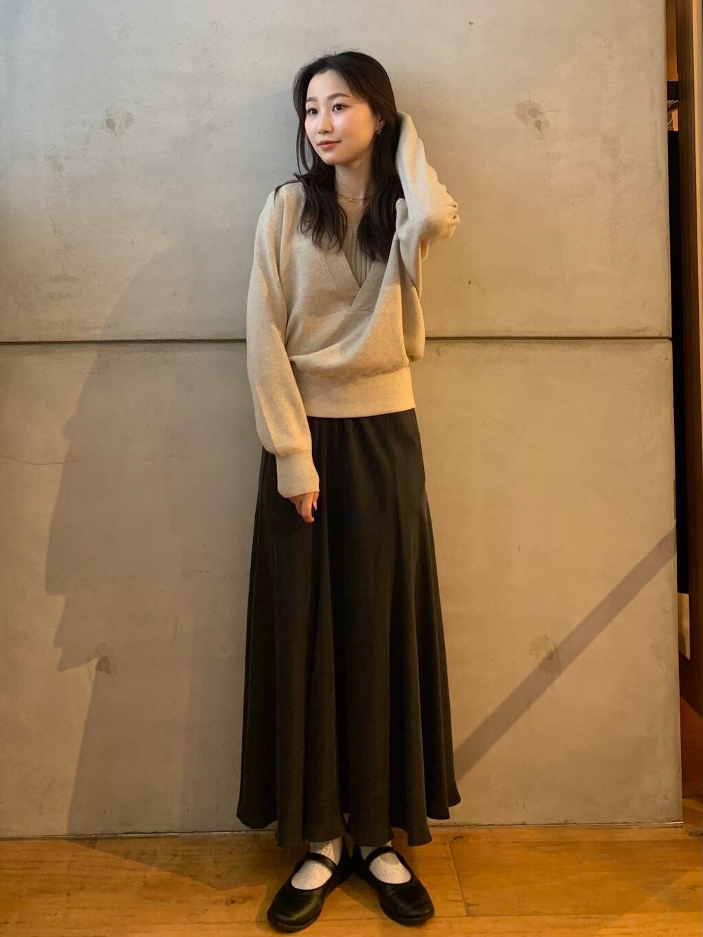 グレー系のスカート、ベージュ系のタンクトップ、ベージュ系のニット/セーターを着用したレディースの秋コーディネートの1枚目の写真