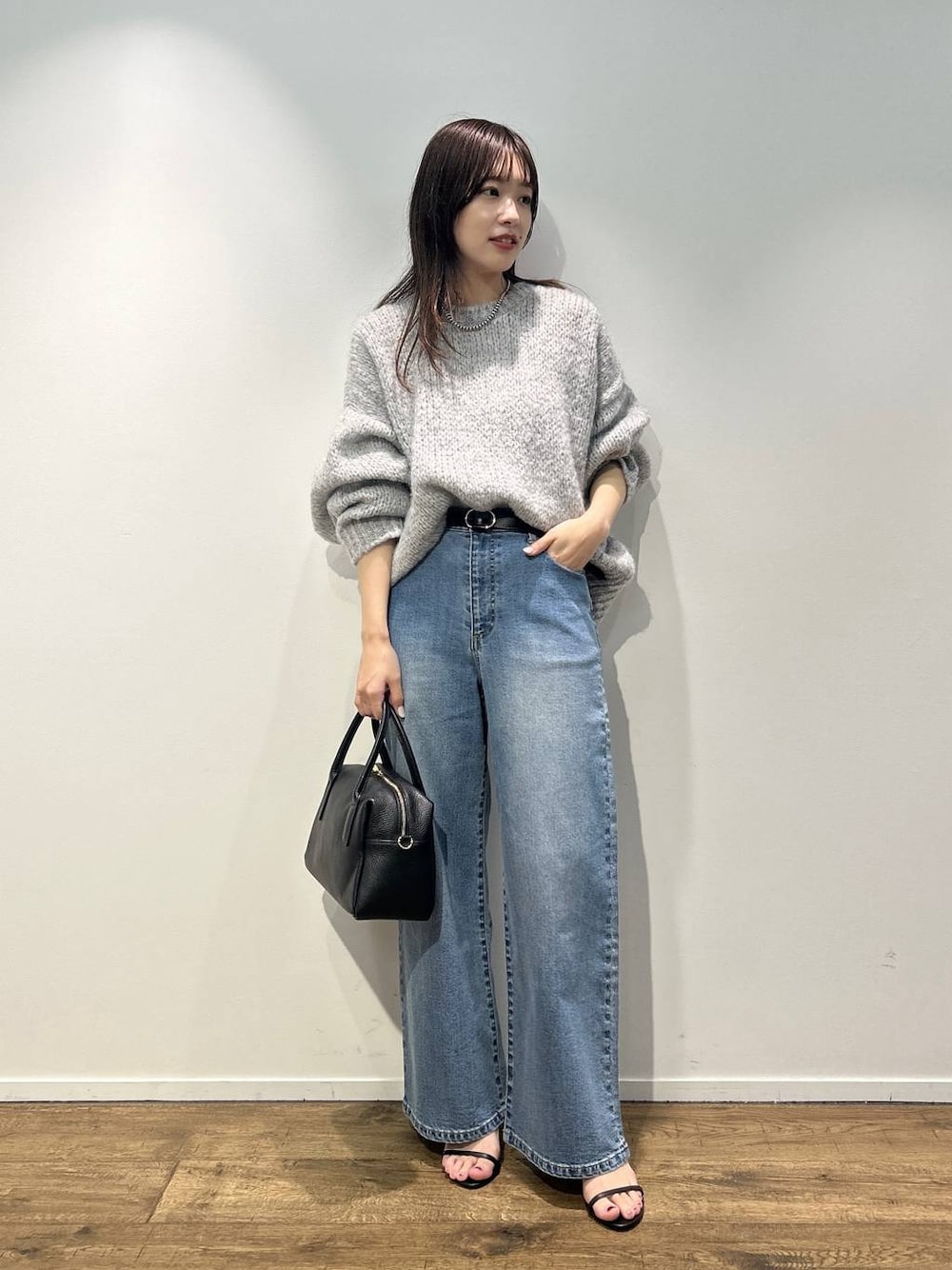 ブラック系のボストンバッグ、ブルー系のデニムパンツ、グレー系のニット/セーターを着用したレディースの秋コーディネートの1枚目の写真