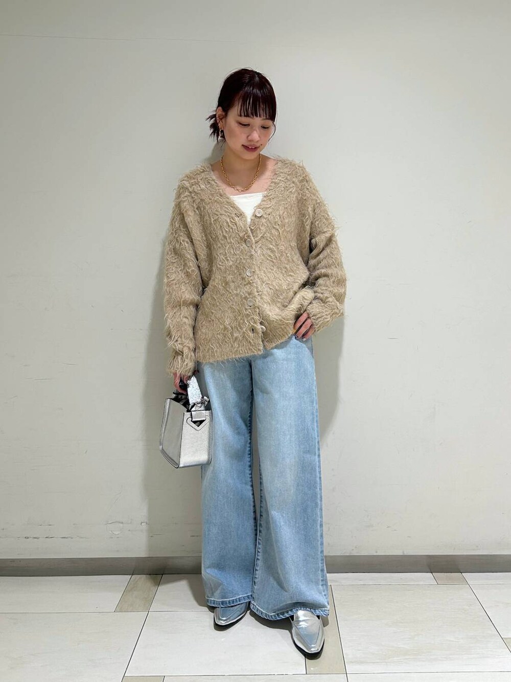 シルバー系のハンドバッグ、シルバー系のローファー、ブルー系のデニムパンツを着用したレディースの冬コーディネートの1枚目の写真