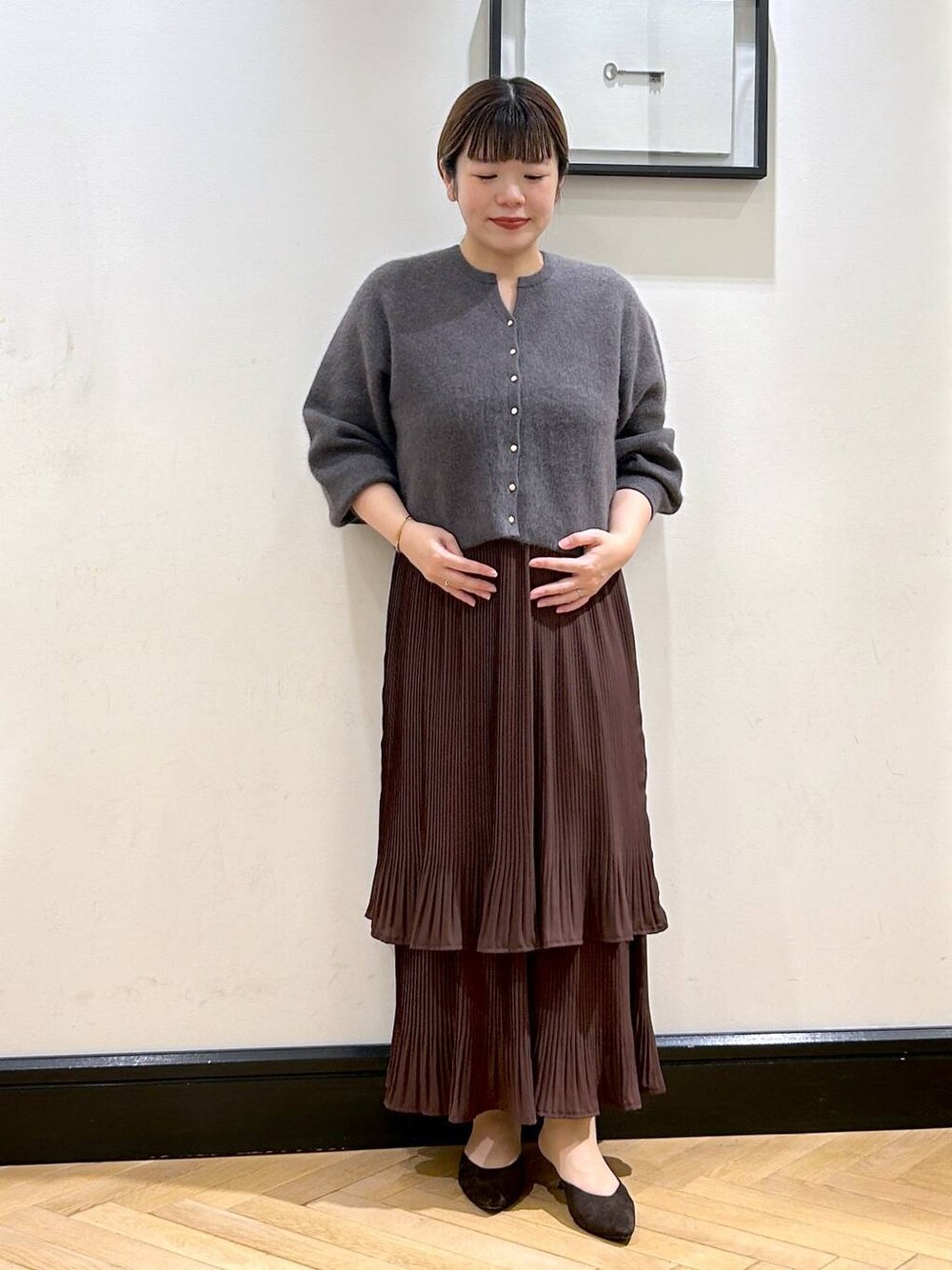 ブラウン系のスカート、グレー系のカーディガン/ボレロ、ブラウン系のパンプスを着用したレディースの秋コーディネートの1枚目の写真