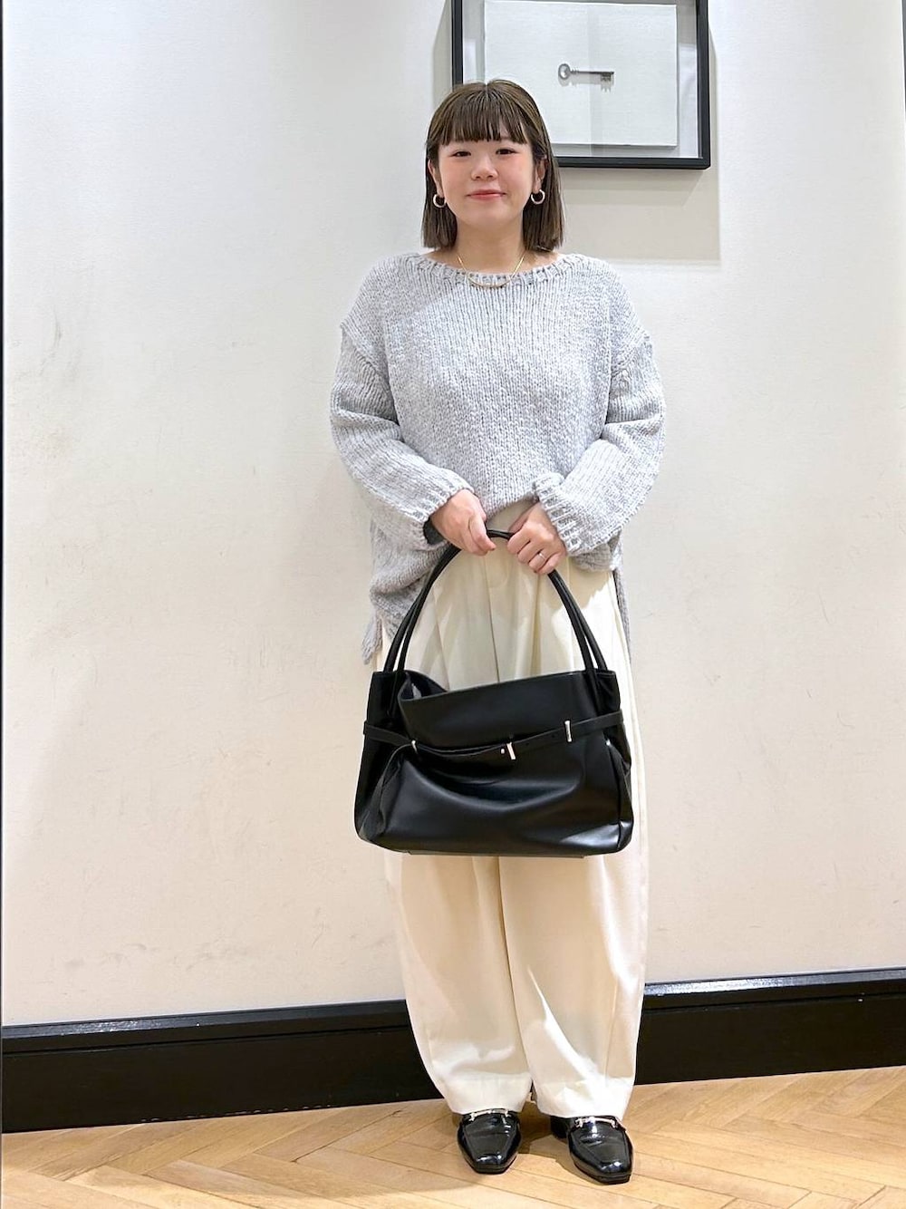 ホワイト系のスラックス、ブラック系のローファー、グレー系のニット/セーターを着用したレディースの秋コーディネートの1枚目の写真