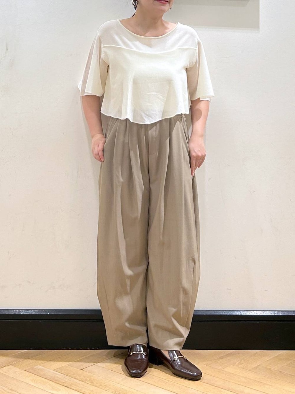 ベージュ系のスラックス、ブラウン系のローファー、ホワイト系のニット/セーターを着用したレディースの夏コーディネートの1枚目の写真