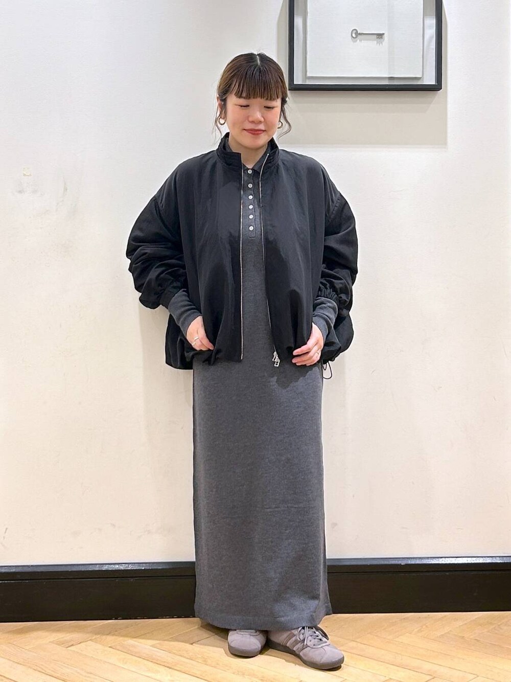 グレー系のスニーカー、グレー系のワンピース、ブラック系のブルゾンを着用したレディースの秋コーディネートの1枚目の写真