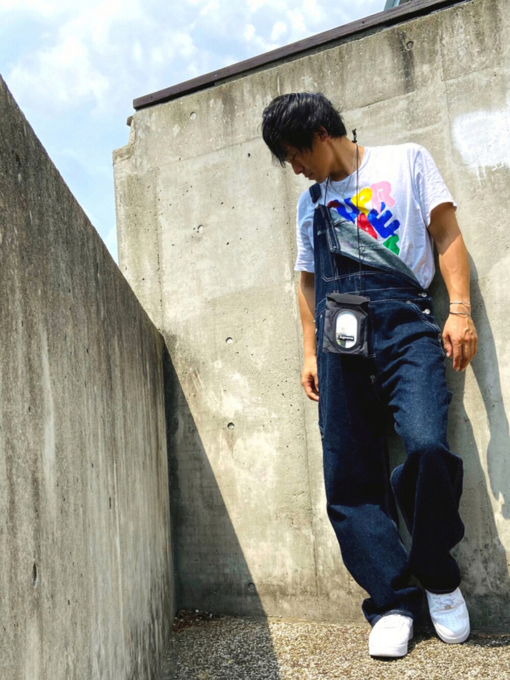 ホワイト系のスニーカー、ブルー系のサロペット/オーバーオール、ブラック系のショルダーバッグを着用したメンズの夏コーディネートの1枚目の写真