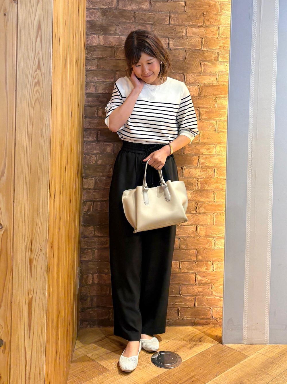 ホワイト系のニット/セーター、ゴールド系のパンプス、グレー系のトートバッグを着用したレディースの夏コーディネートの1枚目の写真