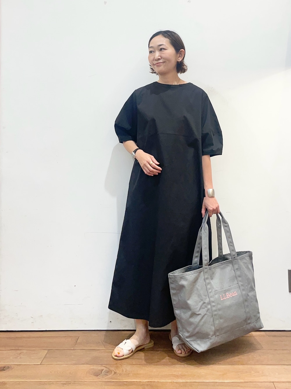 ブラック系のワンピース、ホワイト系のサンダル、グレー系のトートバッグを着用したレディースの春コーディネートの1枚目の写真