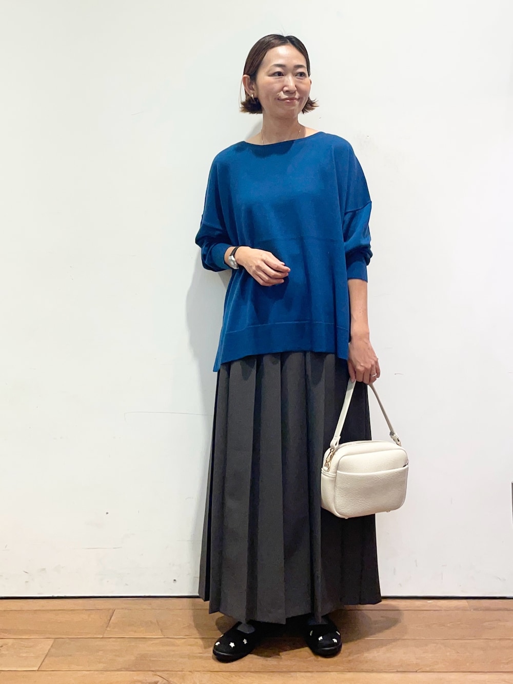 ブルー系のニット/セーター、ブラック系のスニーカー、グレー系のスカートを着用したレディースの秋コーディネートの1枚目の写真