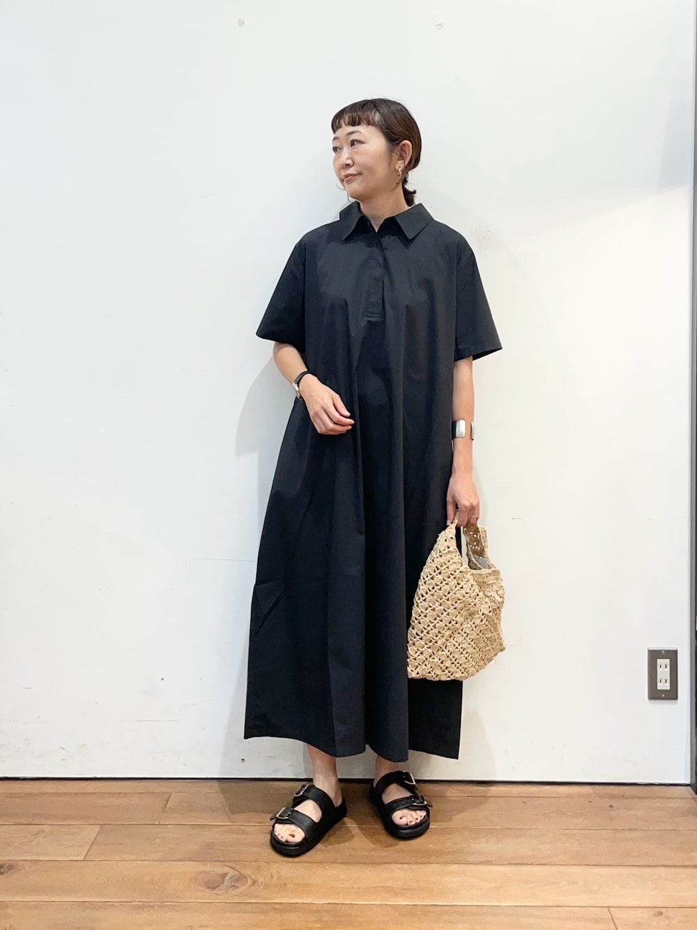 グレー系のワンピース、ベージュ系のハンドバッグ、ブラック系のサンダルを着用したレディースの夏コーディネートの1枚目の写真