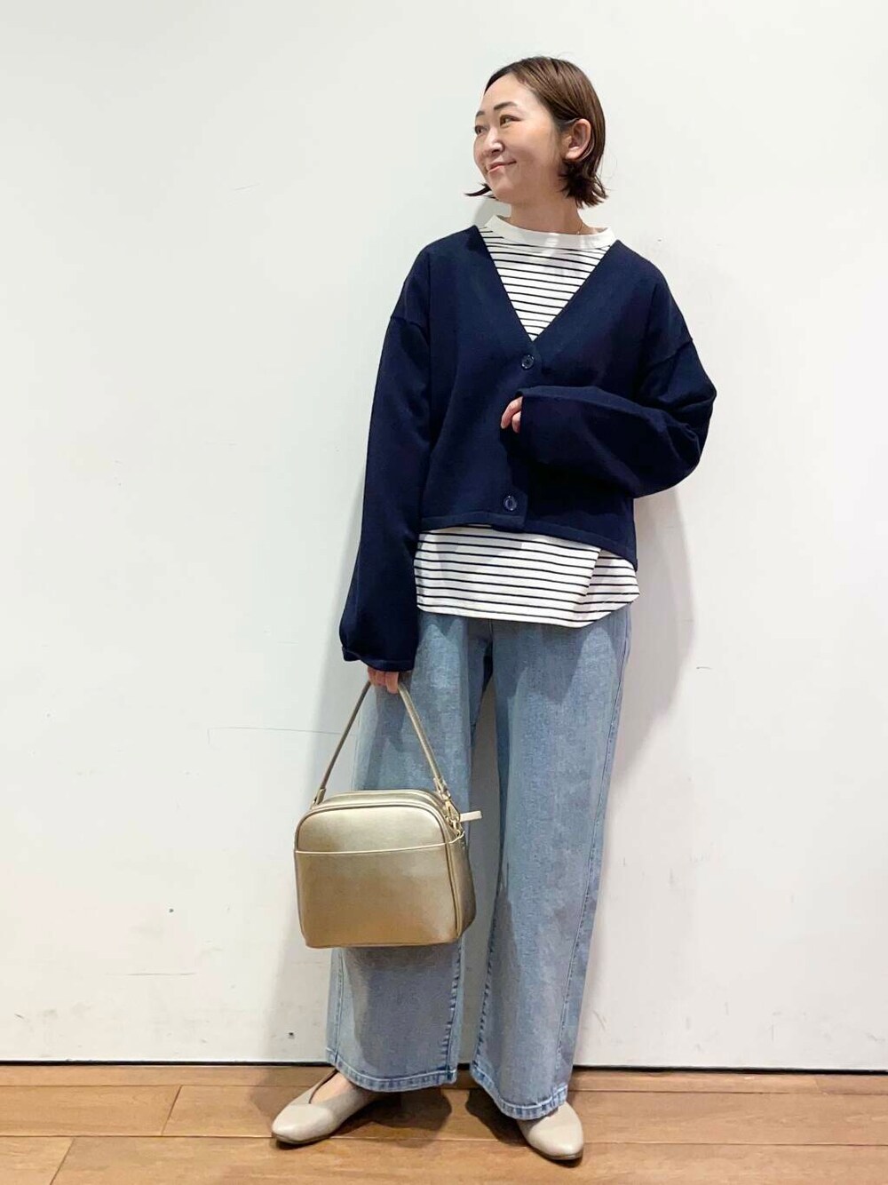 ゴールド系のショルダーバッグ、ブルー系のデニムパンツ、グレー系のパンプスを着用したレディースの冬コーディネートの1枚目の写真